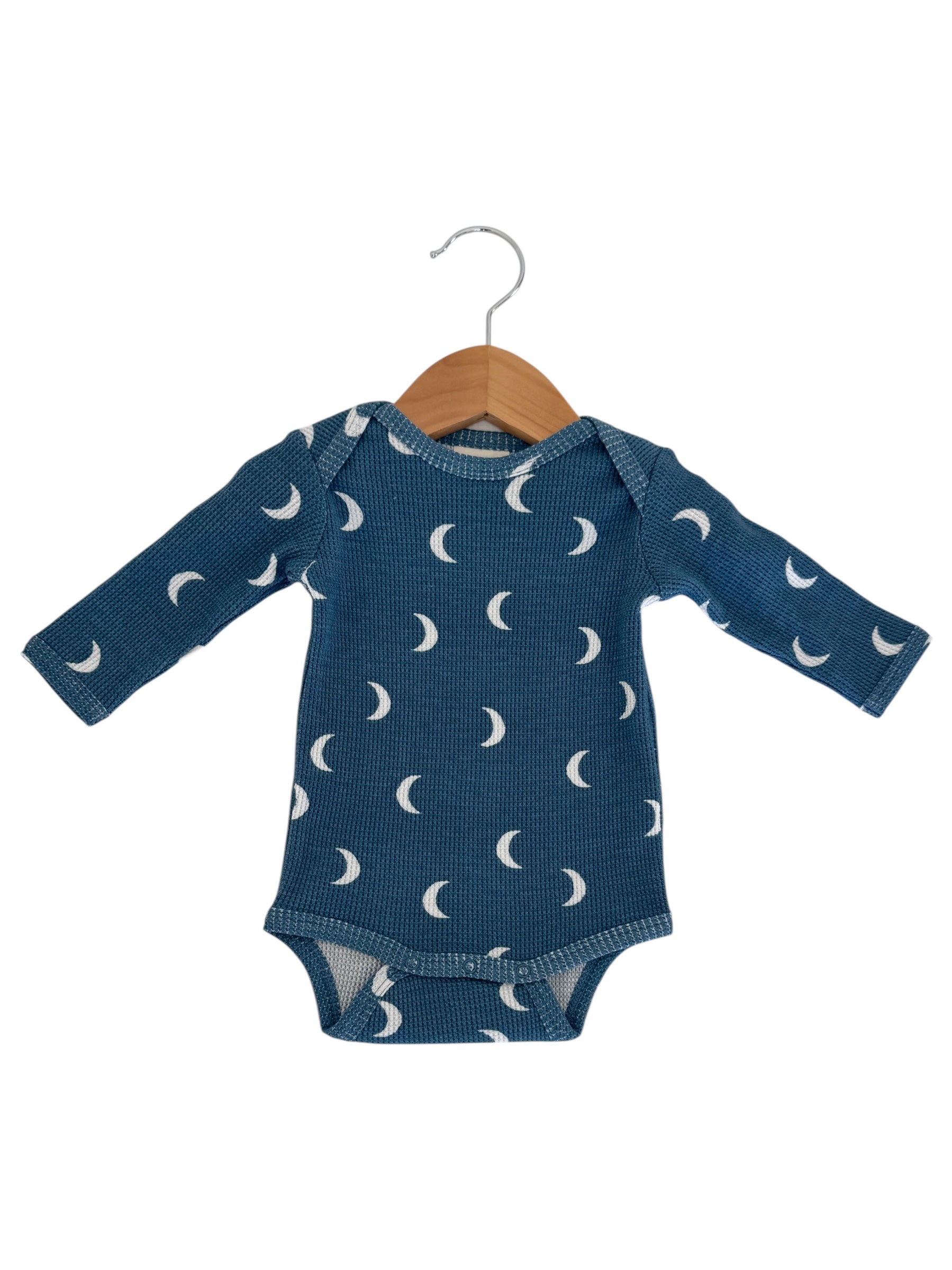 Blue long-sleeve onesie with white crescent moon patterns, hanging on a wooden hanger.
