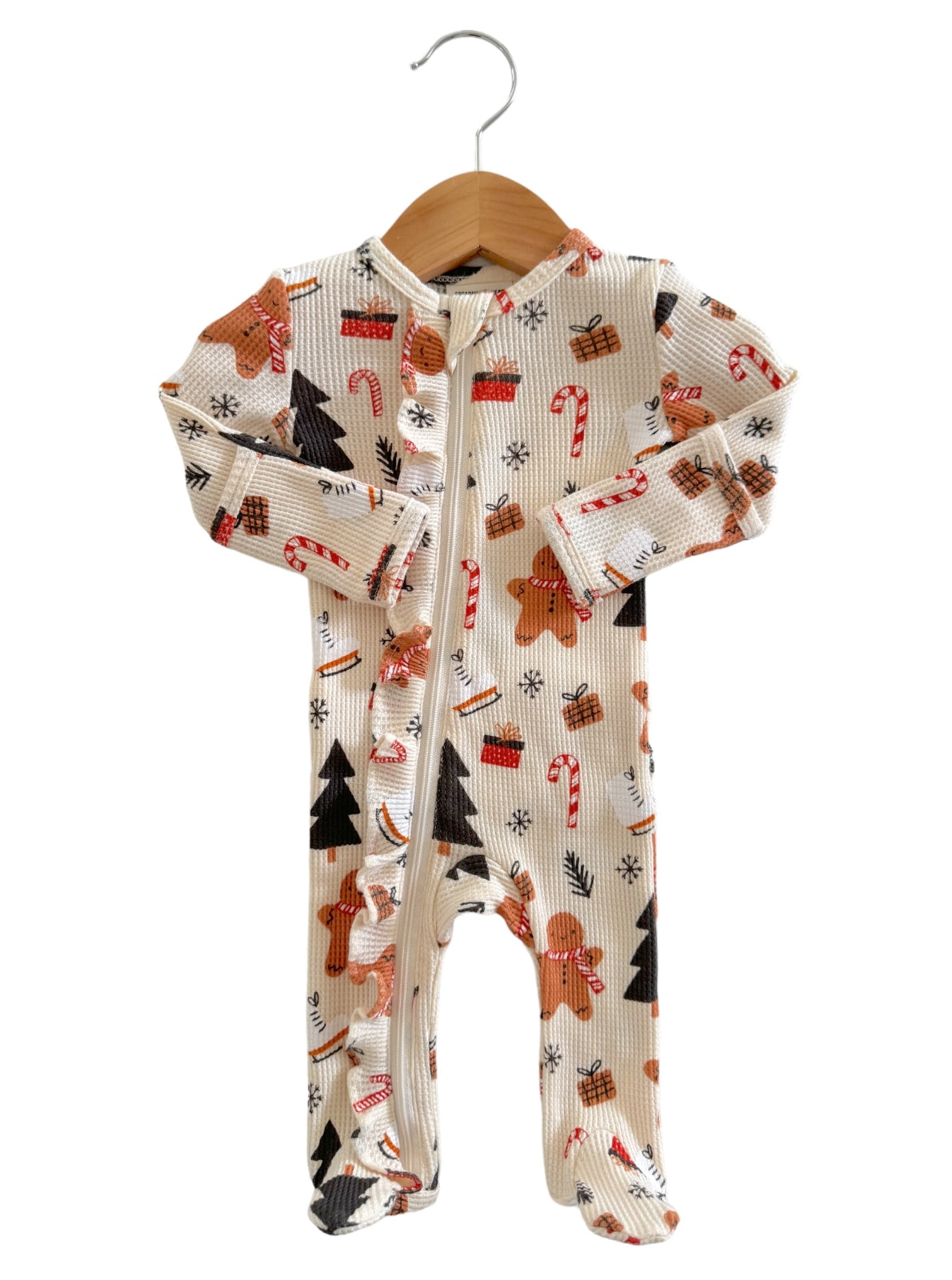 Holiday-themed infant onesie with gingerbread cookies, candy canes, and Christmas trees, hung on a wooden hanger.