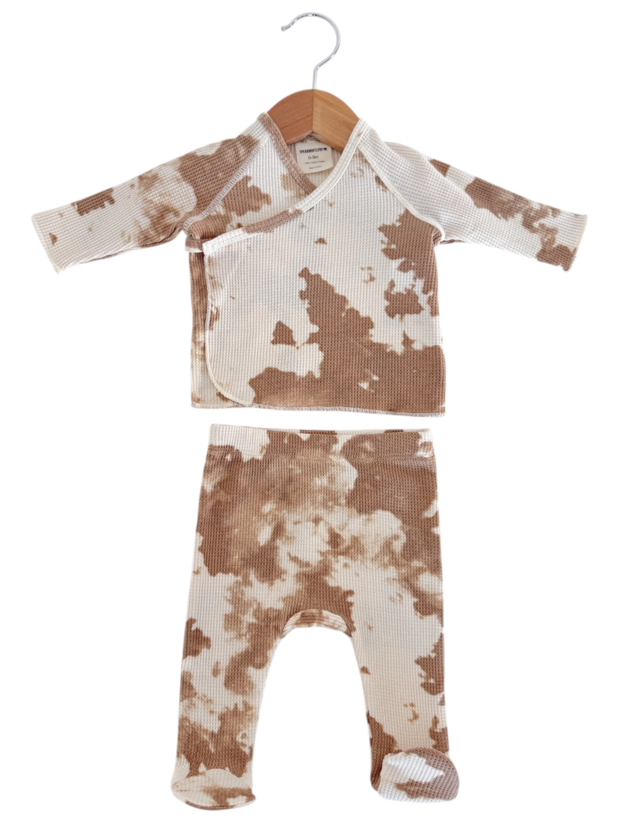 Tan and cream baby pajama set with a patterned top and matching pants, hanging on a wooden hanger.