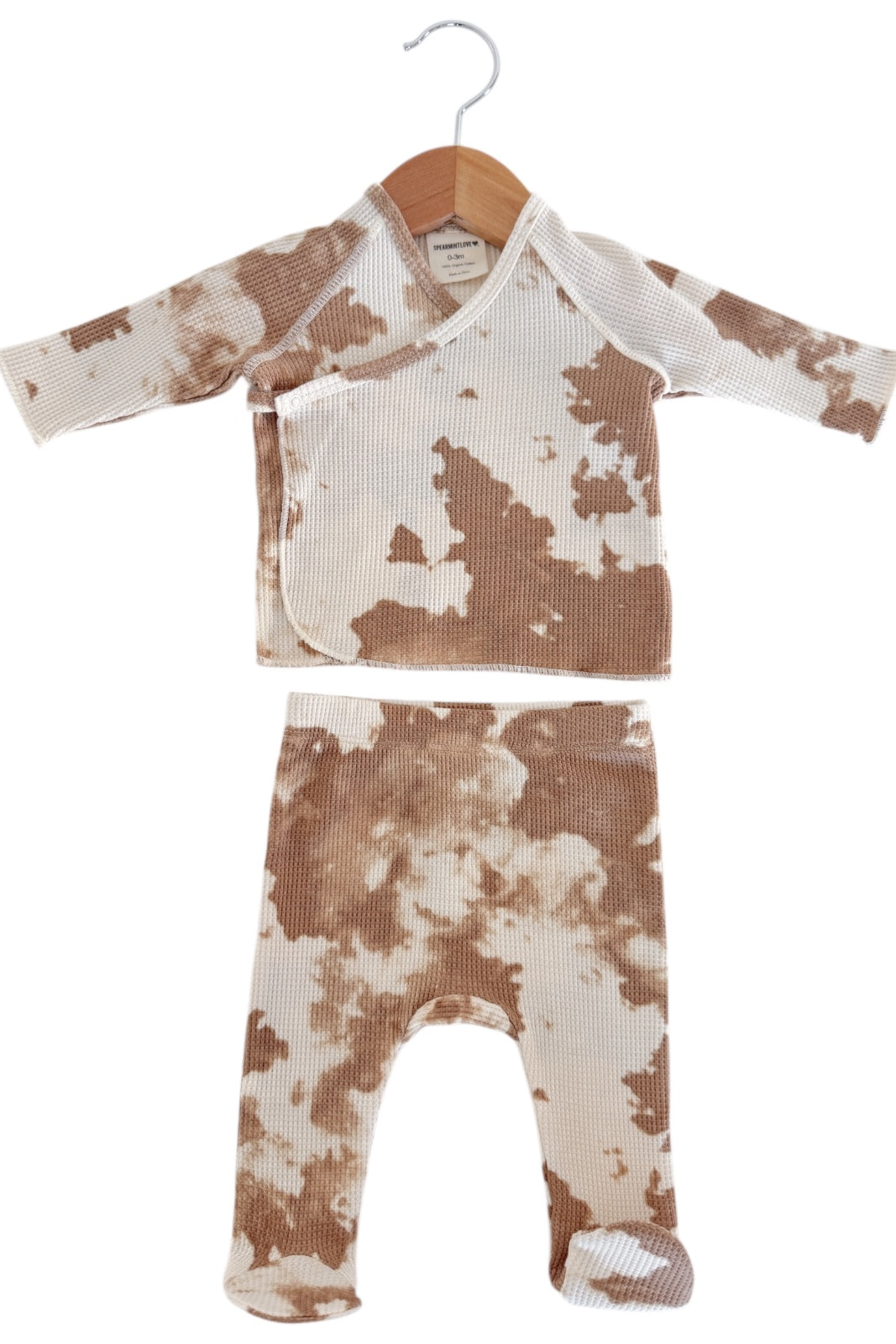 Tan and cream baby pajama set with a patterned top and matching pants, hanging on a wooden hanger.