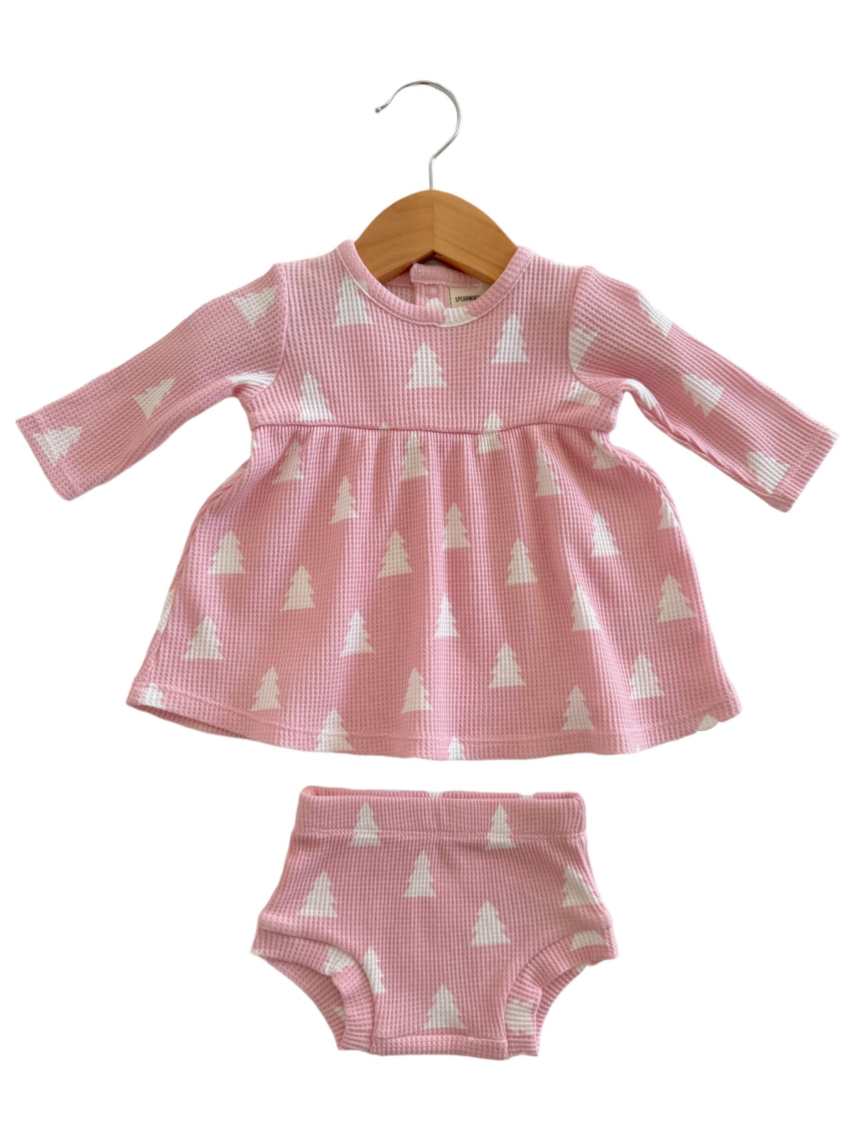Pink children's dress with long sleeves and matching shorts, featuring white triangle patterns, displayed on a hanger.