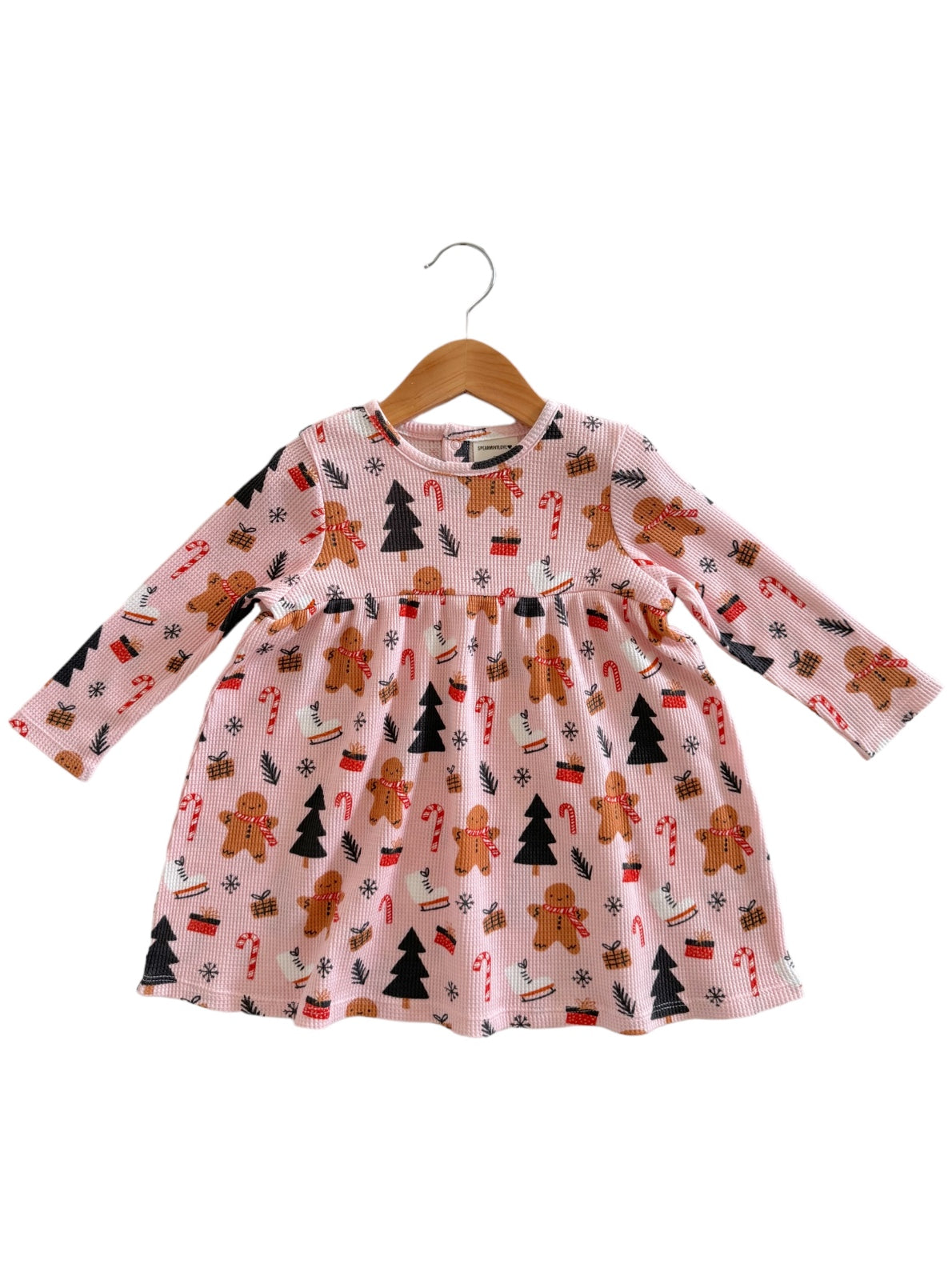Pink dress with gingerbread men, candy canes, and Christmas trees, displayed on a hanger.