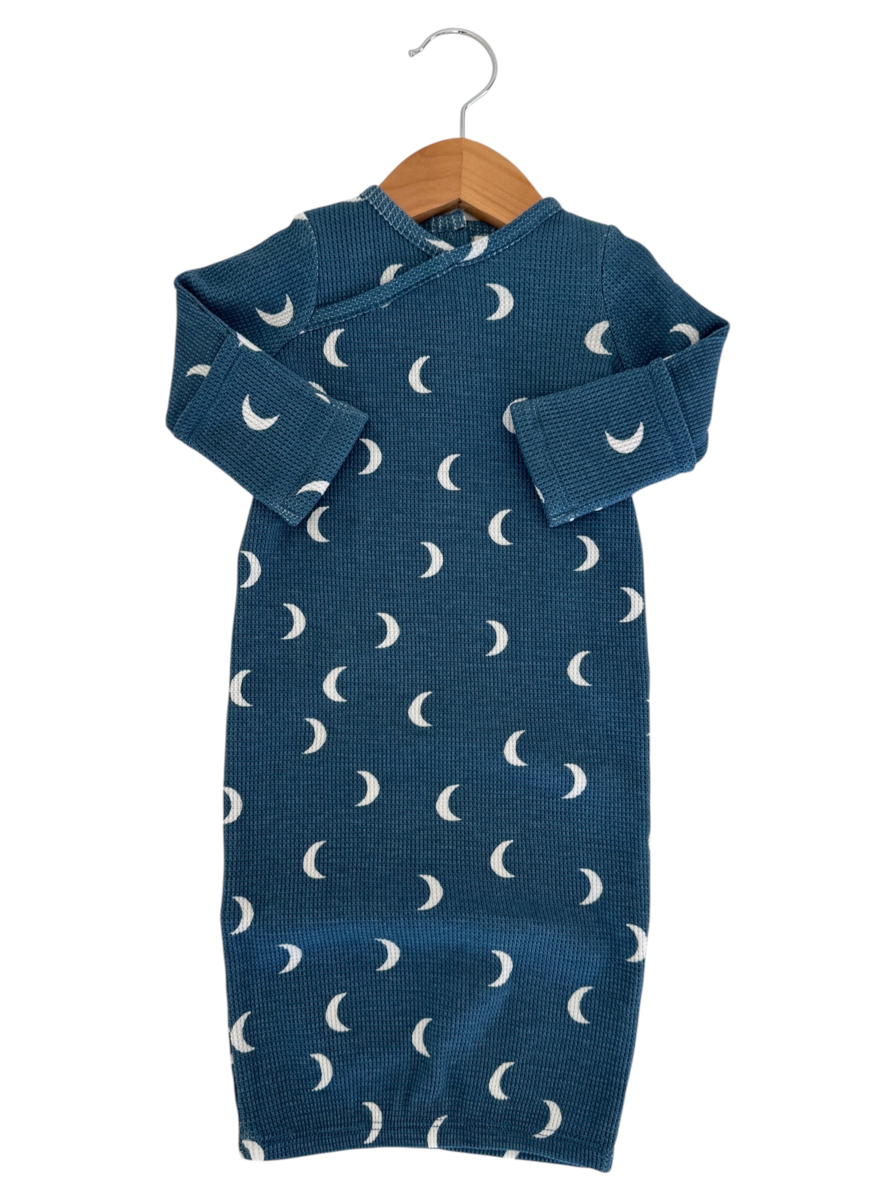 Teal baby dress with white moon patterns, hanging on a wooden hanger against a white background.