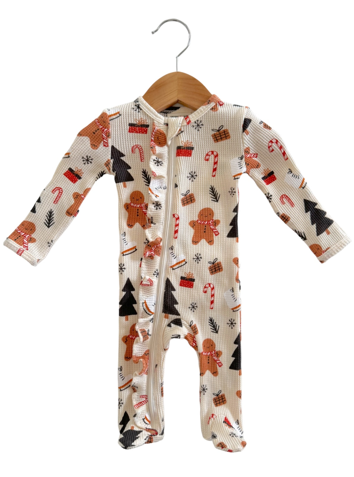 Festive infant onesie with gingerbread men, candy canes, and Christmas trees on a cream background, hanging on a hook.