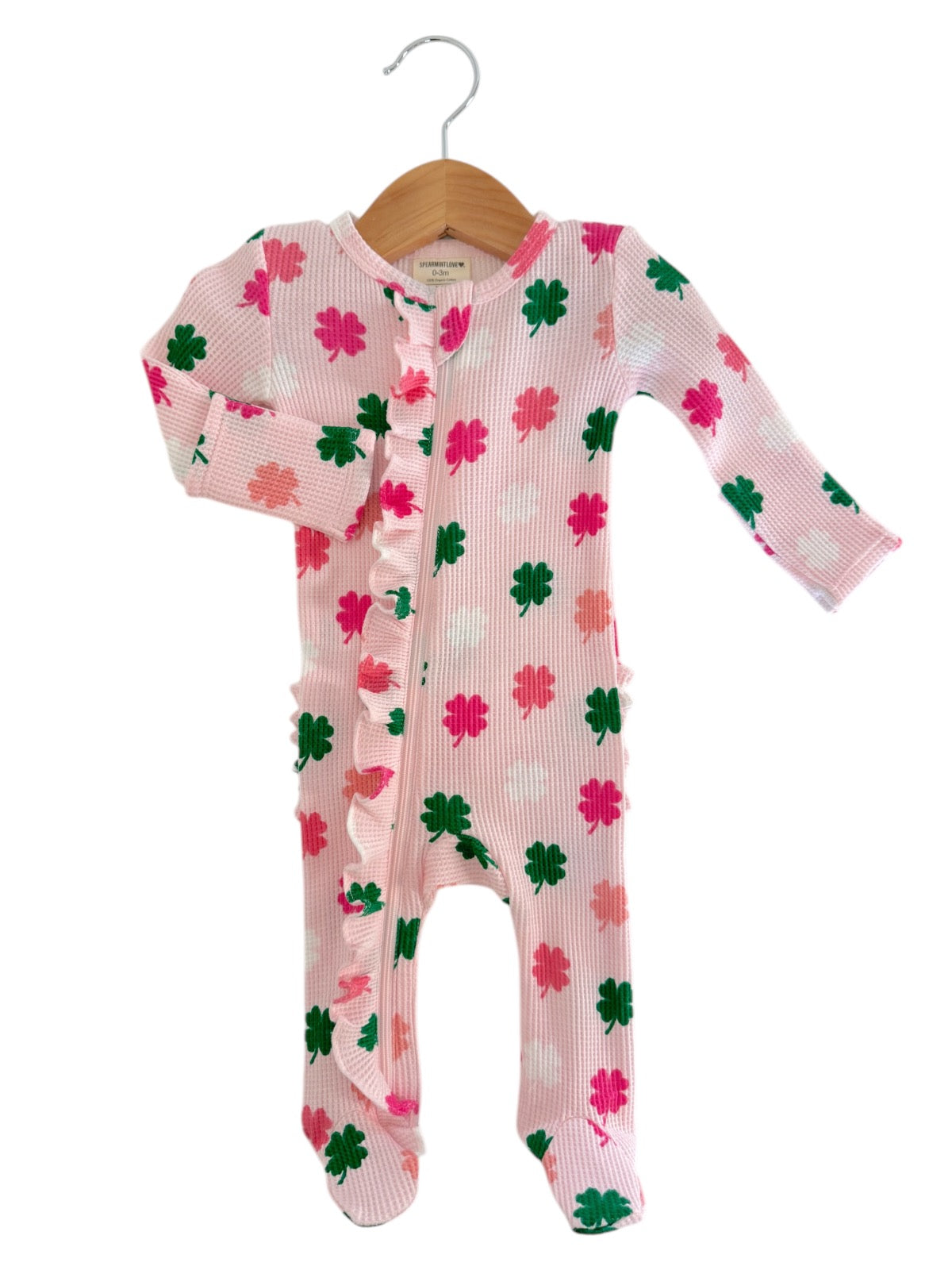 Pink baby onesie with green and pink flower patterns, featuring a ruffled front and long sleeves, hanging on a wooden hanger.