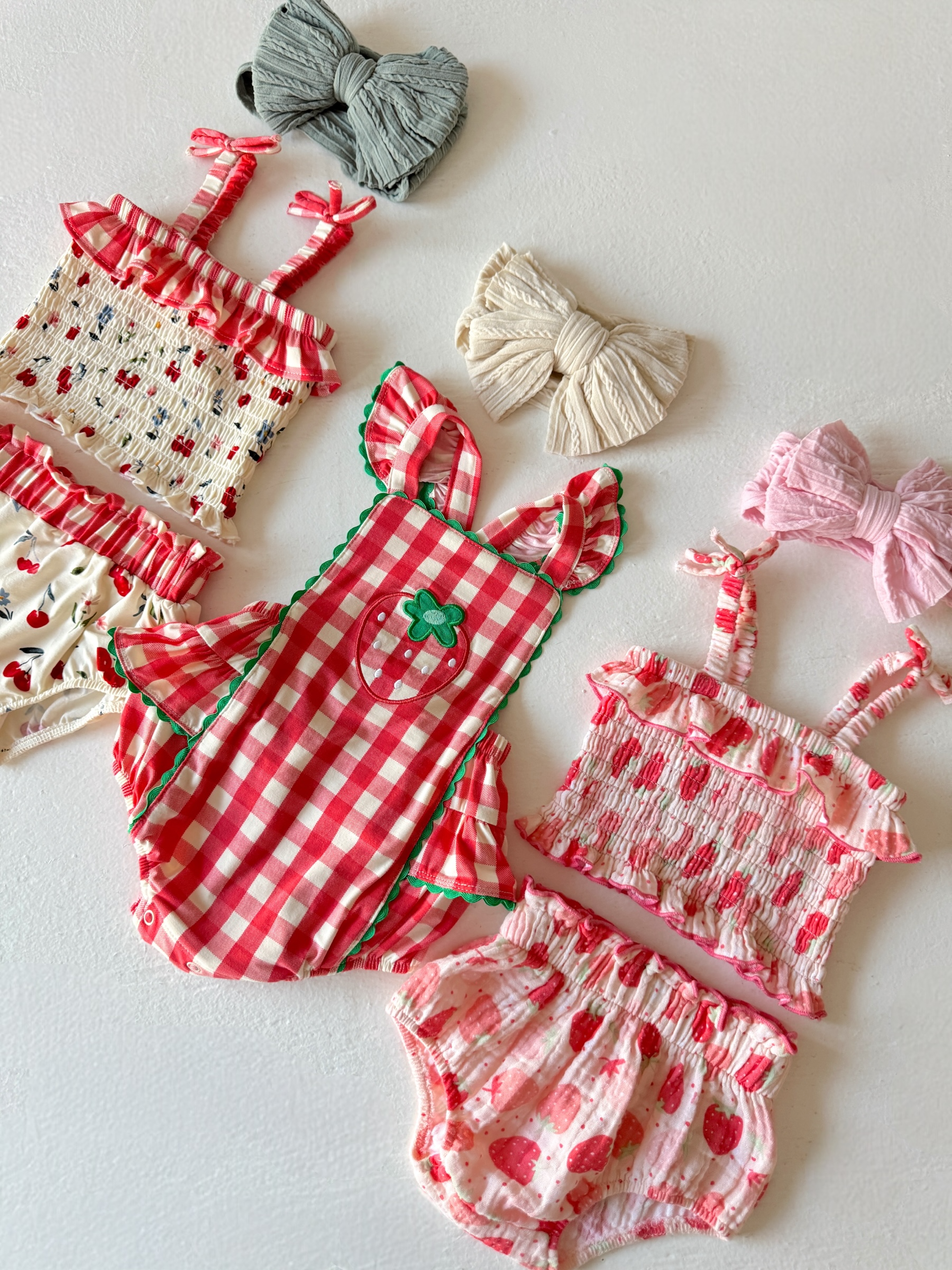Colorful toddler outfits and hair accessories featuring strawberry patterns and frills on a white background.