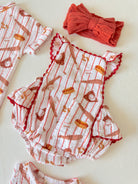 Two toddler rompers with a red and white food pattern, and a matching red headband displayed on a light background.