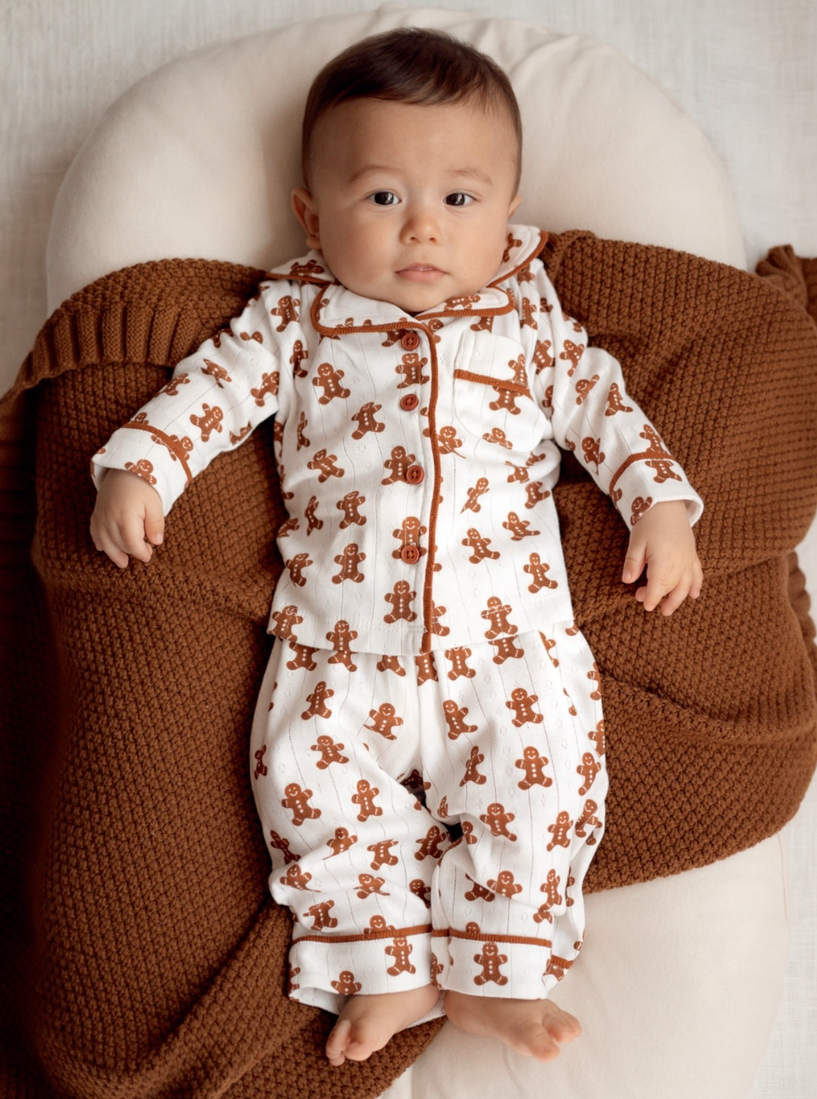 Baby in gingerbread-patterned pajamas, resting on a cozy brown blanket.