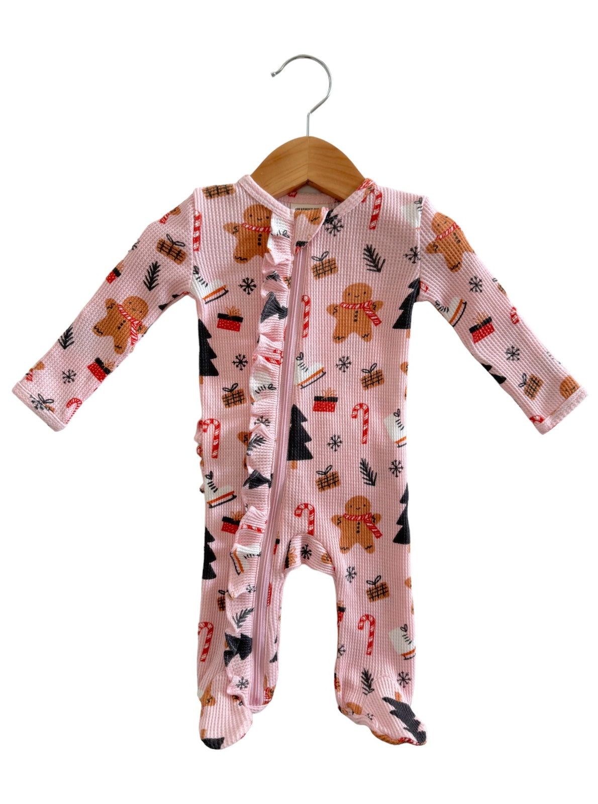 Pink baby onesie featuring gingerbread men, candy canes, and Christmas trees, displayed on a wooden hanger.