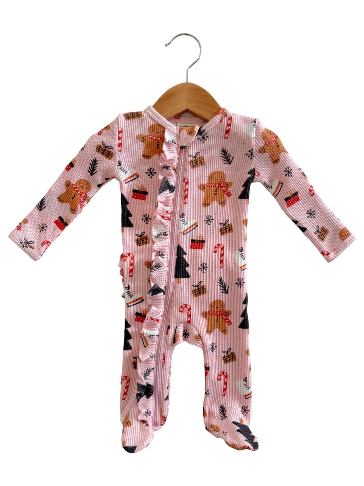 Pink baby onesie featuring gingerbread men, candy canes, and Christmas trees, displayed on a wooden hanger.