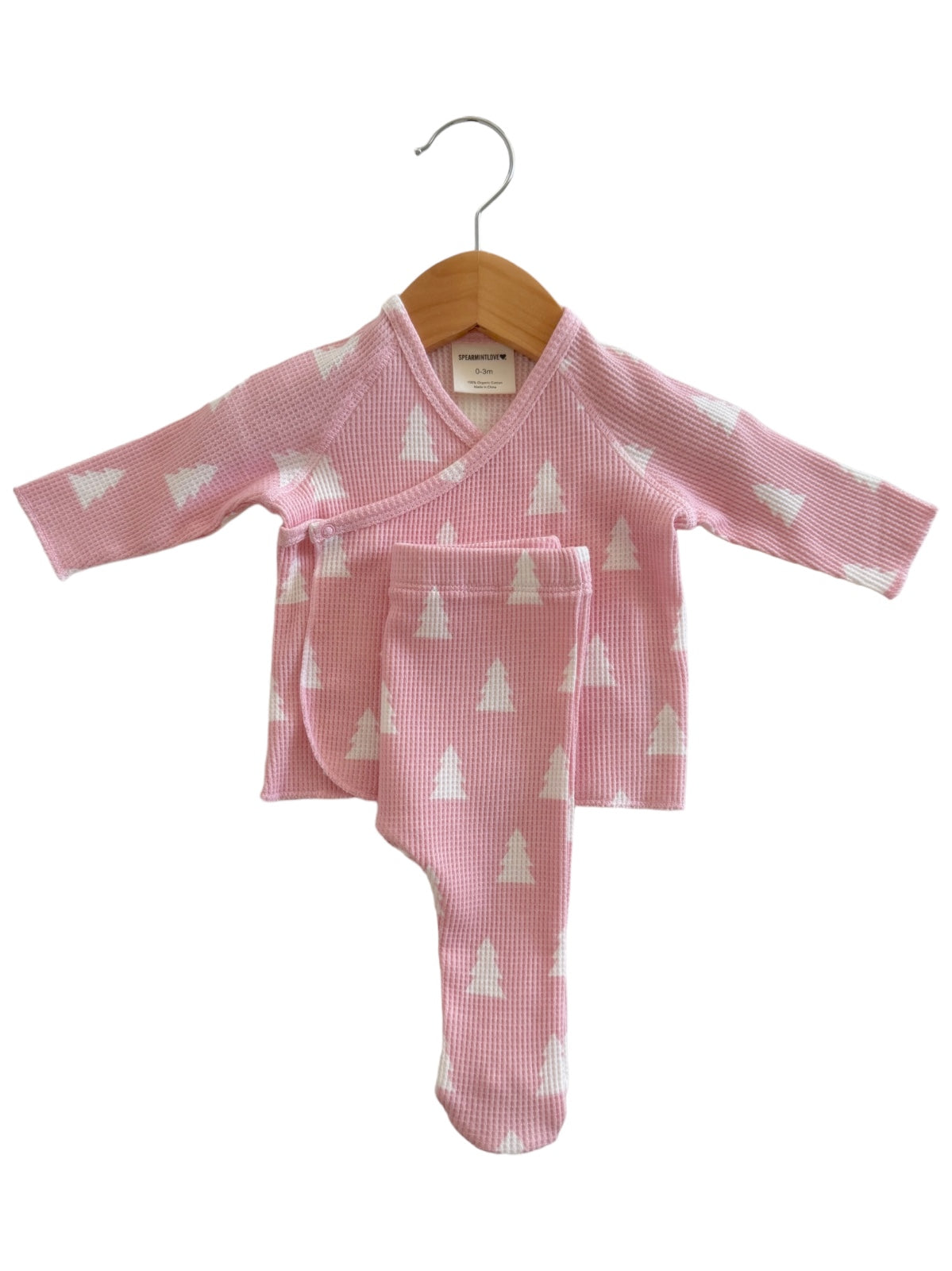 Pink baby outfit with long sleeves and footed pants, featuring white tree patterns, displayed on a wooden hanger.