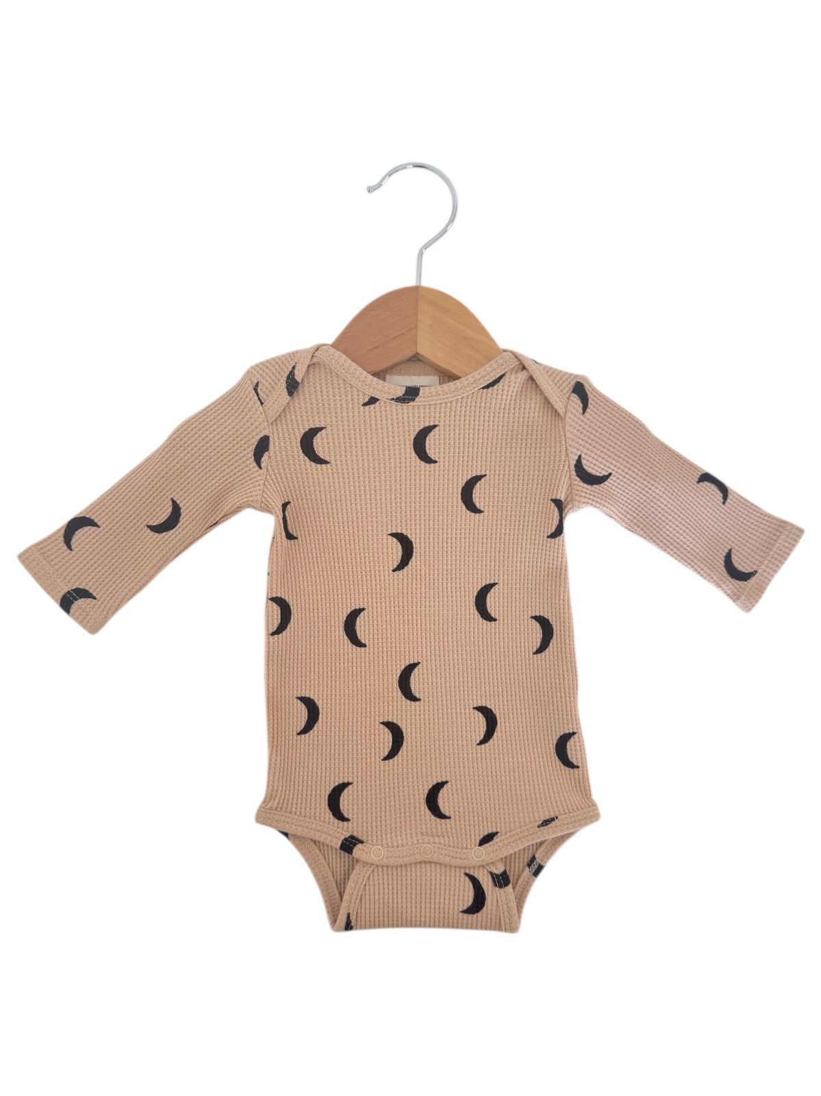 Beige baby onesie with long sleeves and black crescent moon patterns, hanging on a wooden hanger.