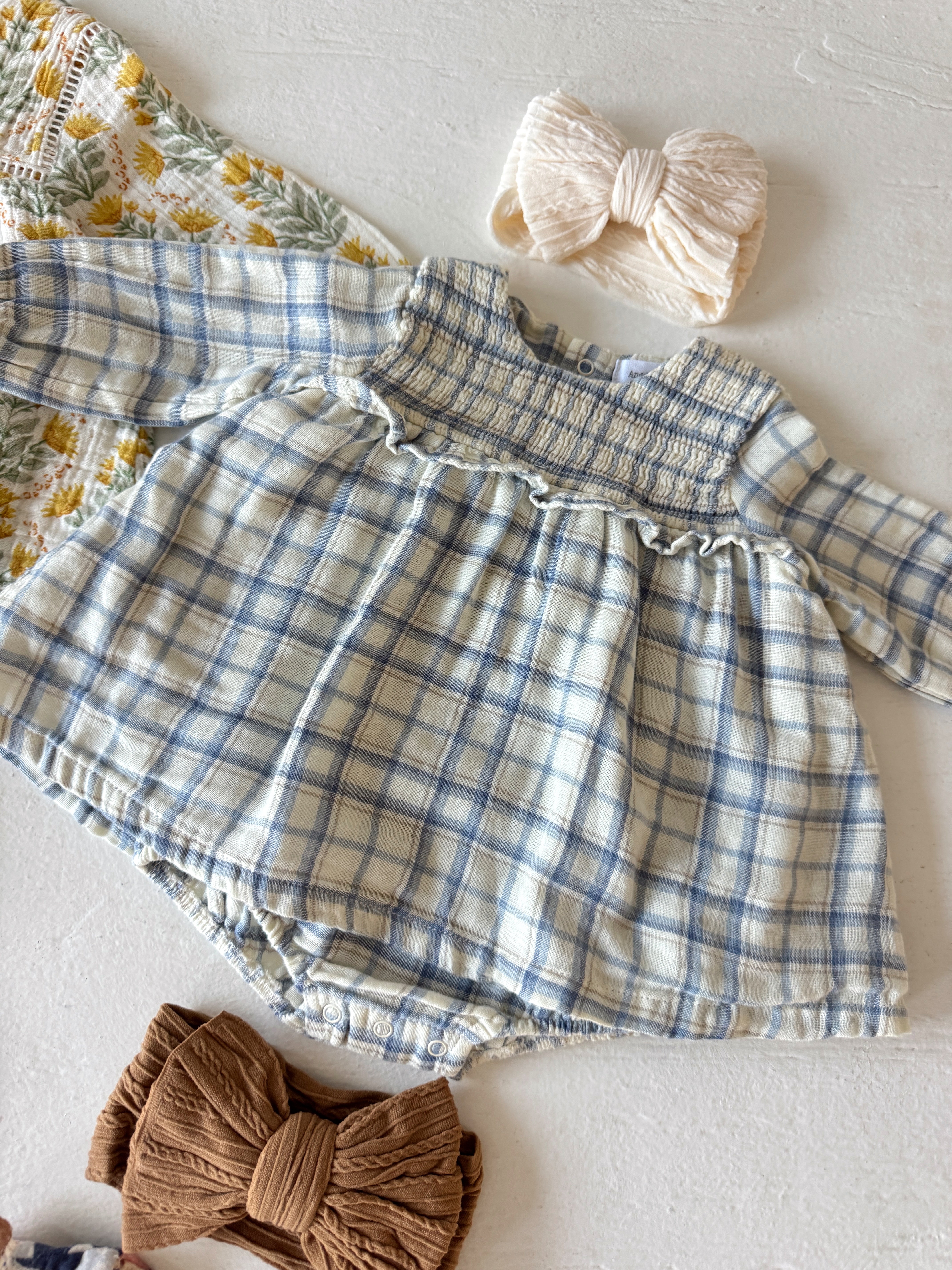 Blue plaid baby dress with matching hair bows on a textured white surface.