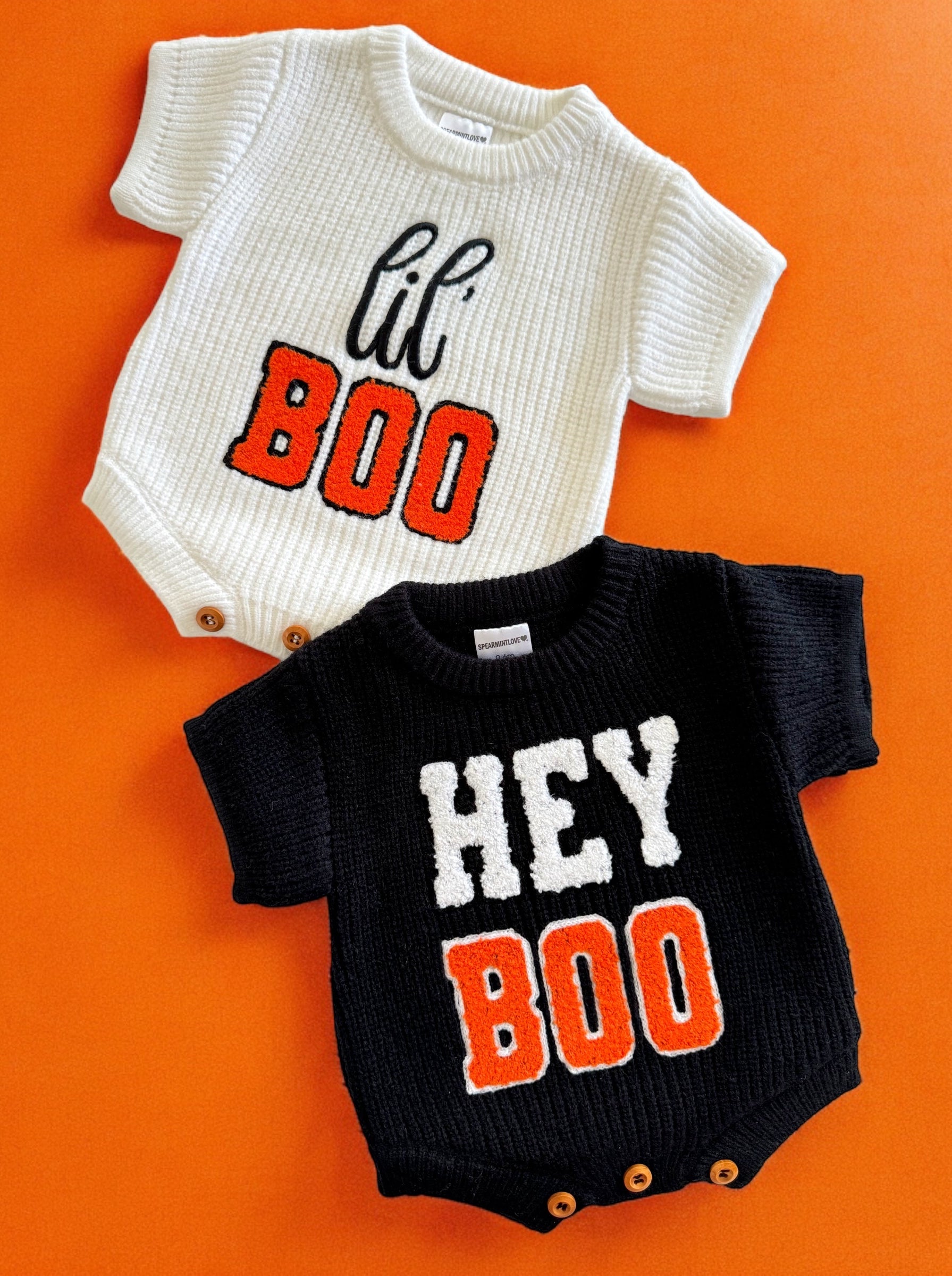 Two short-sleeve baby onesies in white and black, featuring "lil' BOO" and "HEY BOO" text. Bright orange background.