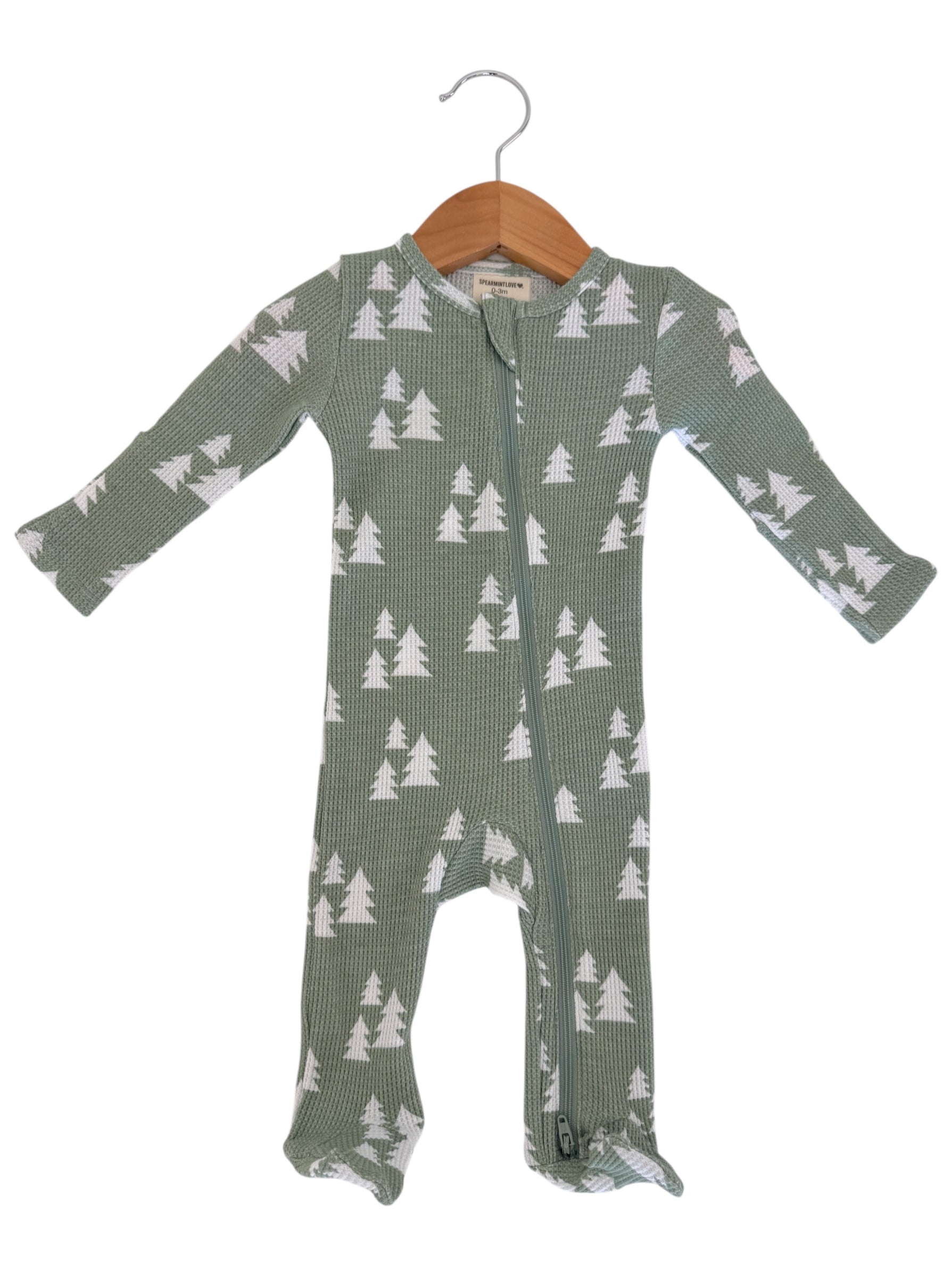 Green cozy baby onesie with white tree pattern, displayed on a wooden hanger.