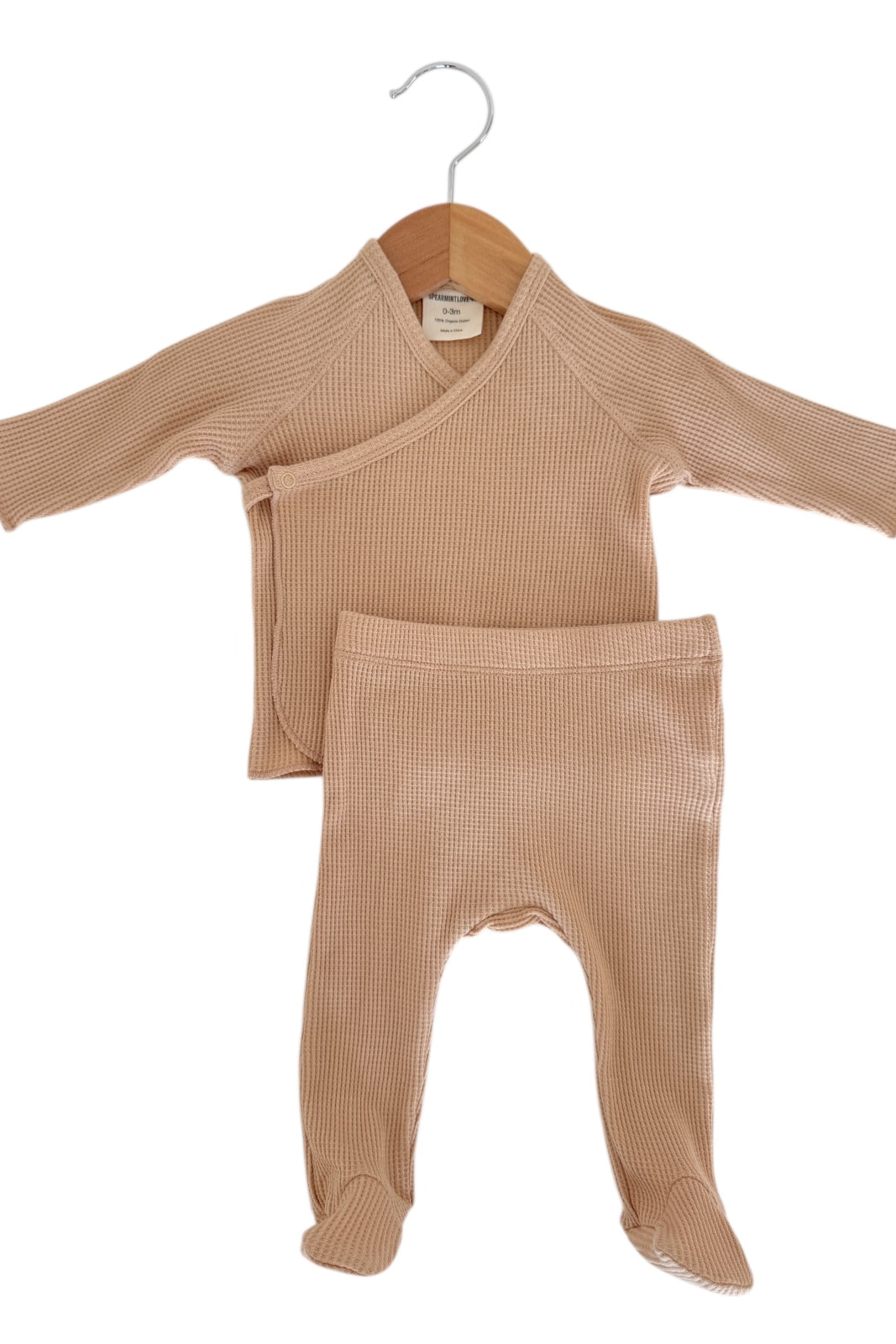 Light brown infant two-piece outfit with a wrap top and footed pants, displayed on a wooden hanger.