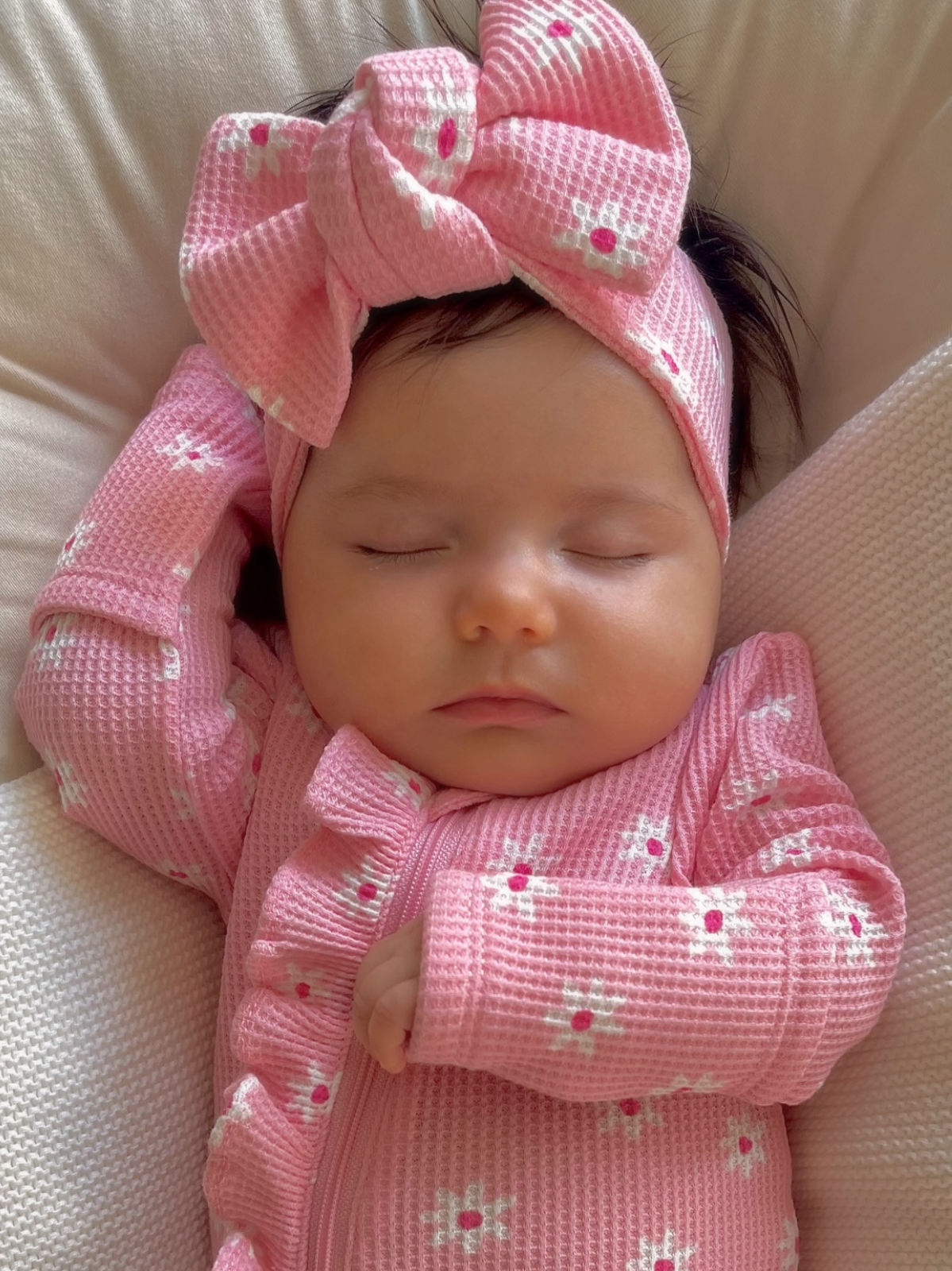 Sleeping baby girl in a pink floral outfit with a large bow headband, resting peacefully.