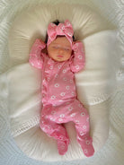 Baby girl in pink floral pajamas and bow, peacefully sleeping on a soft, white pillow.
