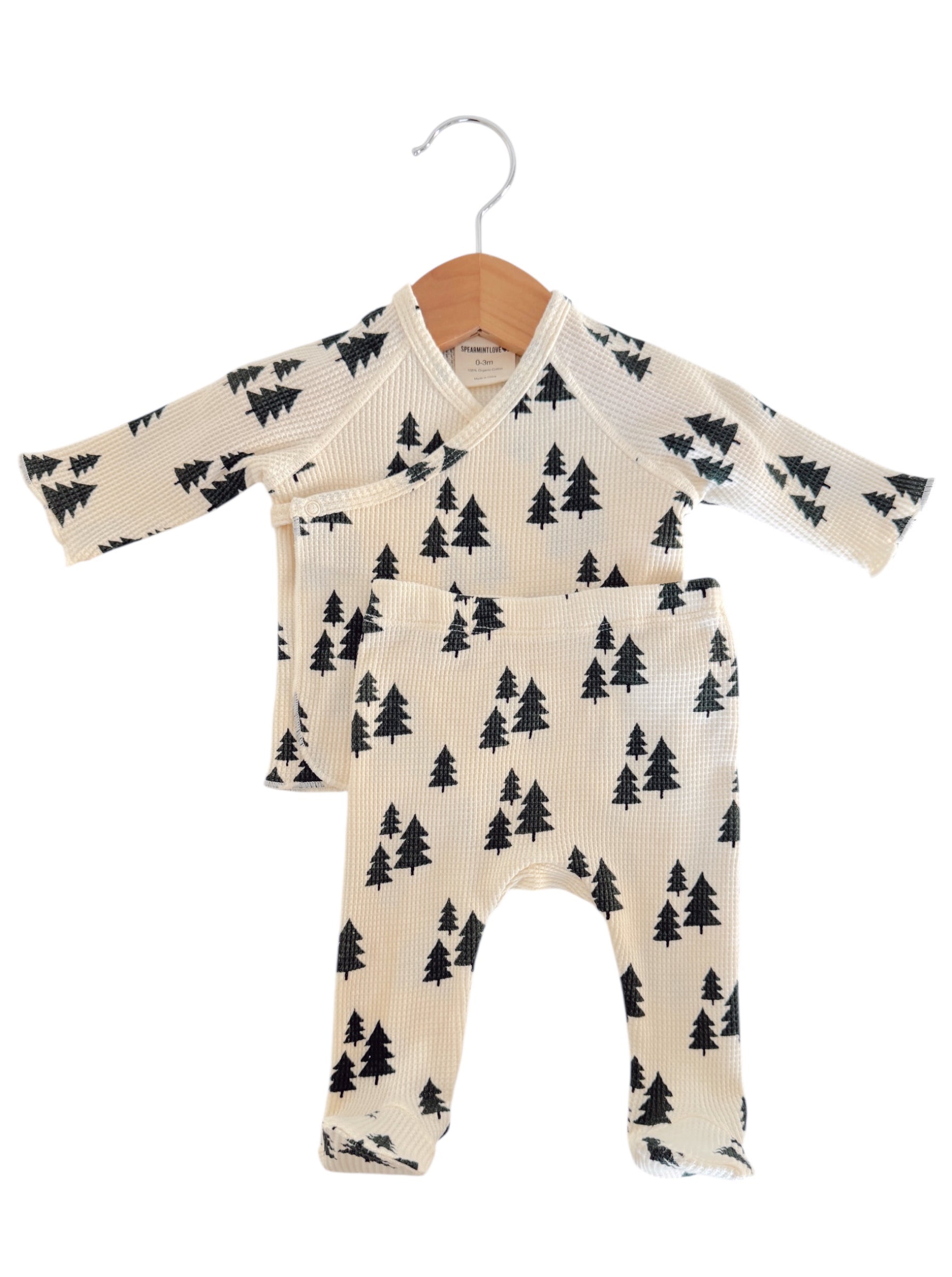 Baby outfit set featuring cream top and pants with black tree print, hanging on a wooden hanger.