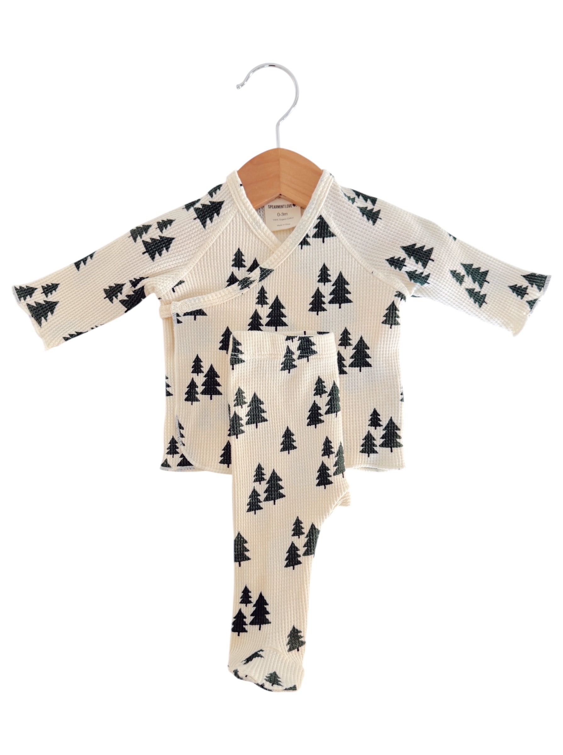 Cream-colored children's pajama set with a tree pattern, displayed on a wooden hanger.