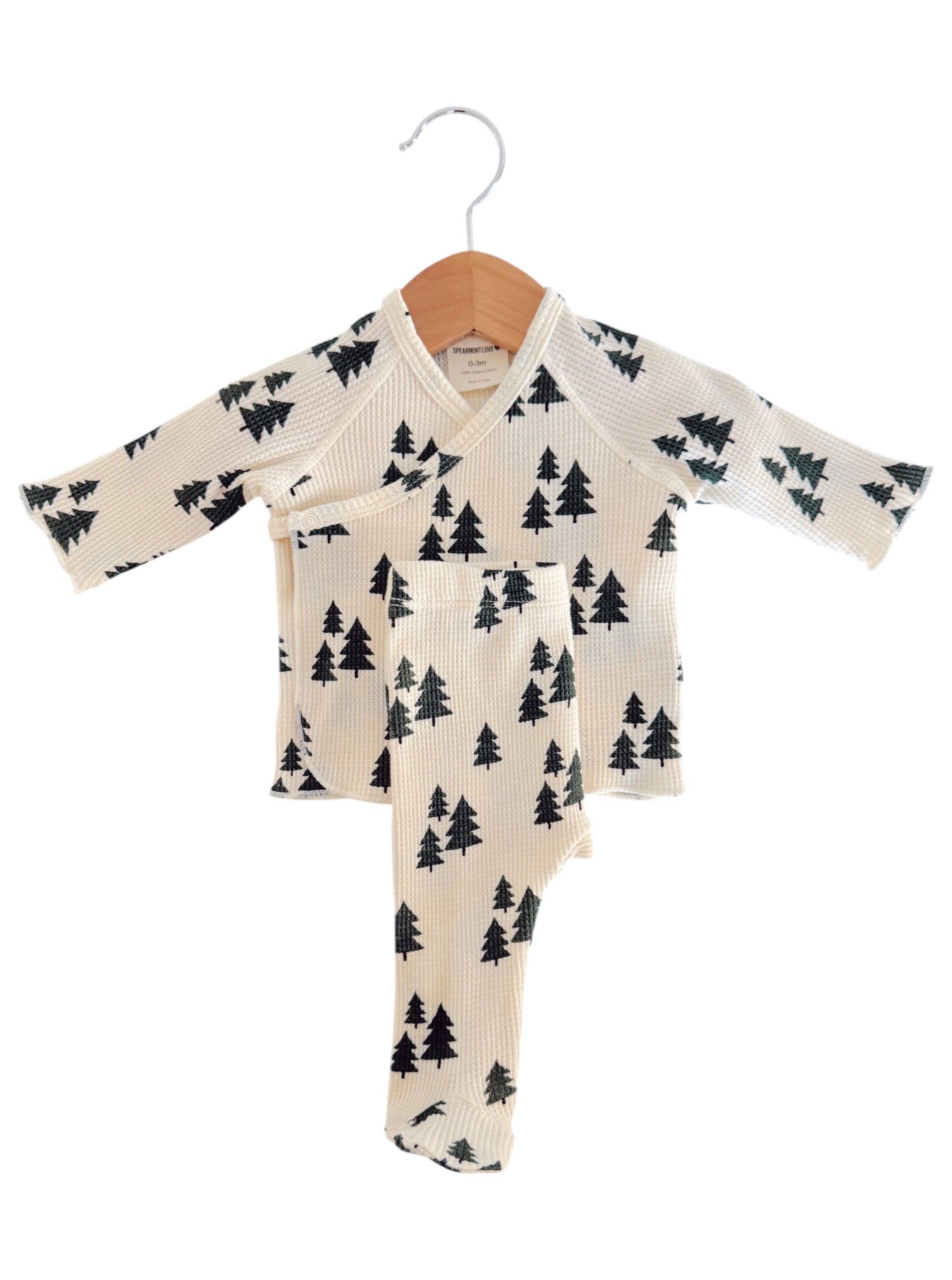 Cream-colored children's pajama set with a tree pattern, displayed on a wooden hanger.
