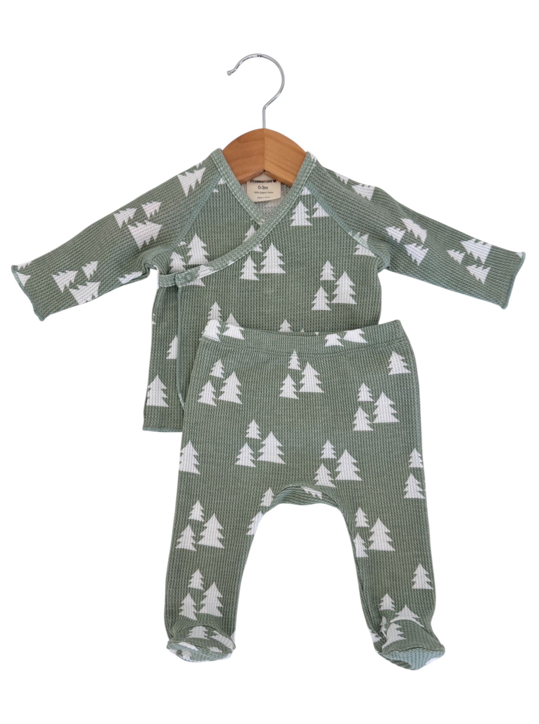 Baby outfit featuring a green pattern with white trees, hanging on a wooden hanger. Size: 0-3 months.
