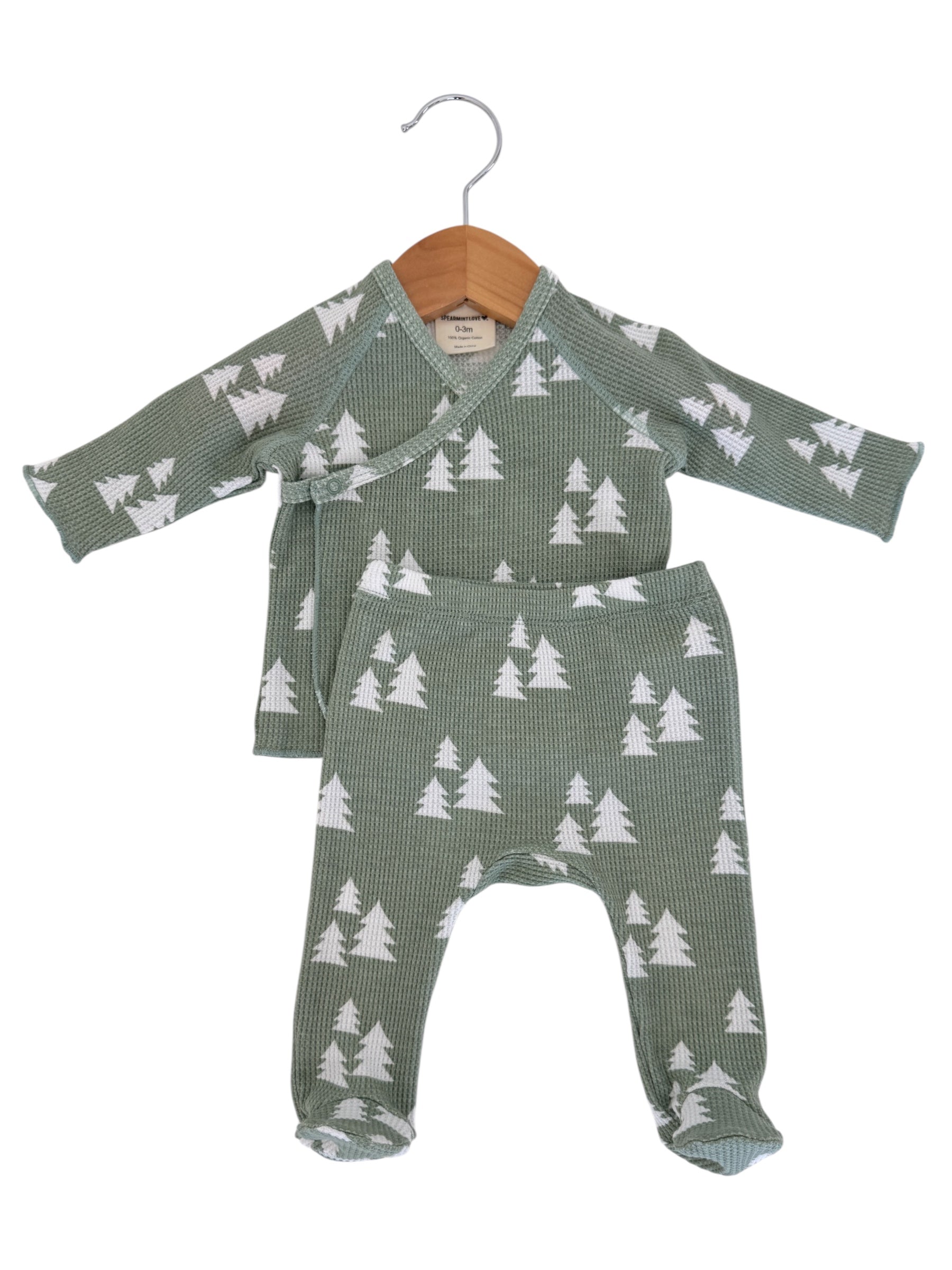 Baby outfit featuring a green pattern with white trees, hanging on a wooden hanger. Size: 0-3 months.