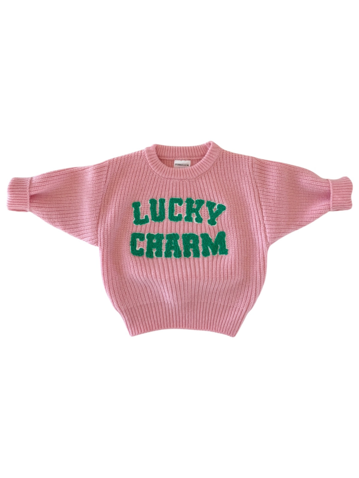 Pink sweater with "LUCKY CHARM" in green lettering on the front, featuring a loose, cozy fit.