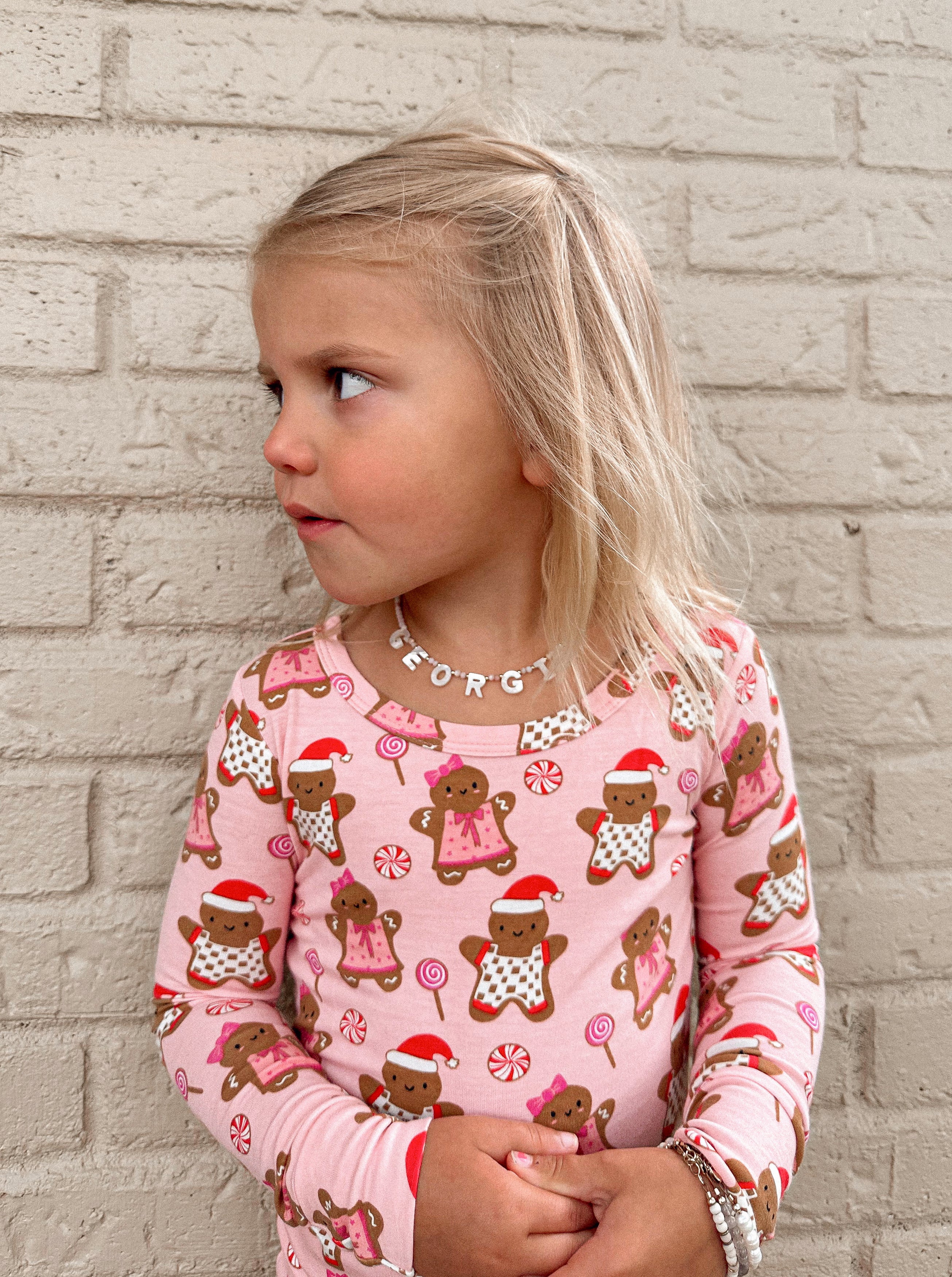 Young girl in a pink gingerbread-patterned shirt, looking sideways against a brick wall background.