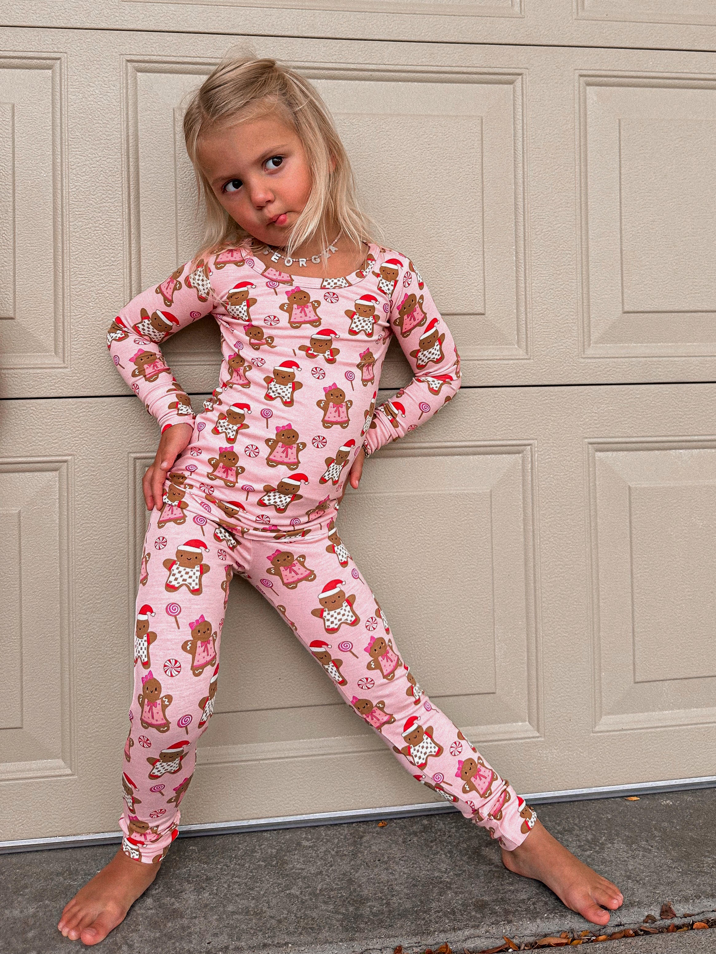Young girl in festive gingerbread pajamas poses playfully against a garage door.