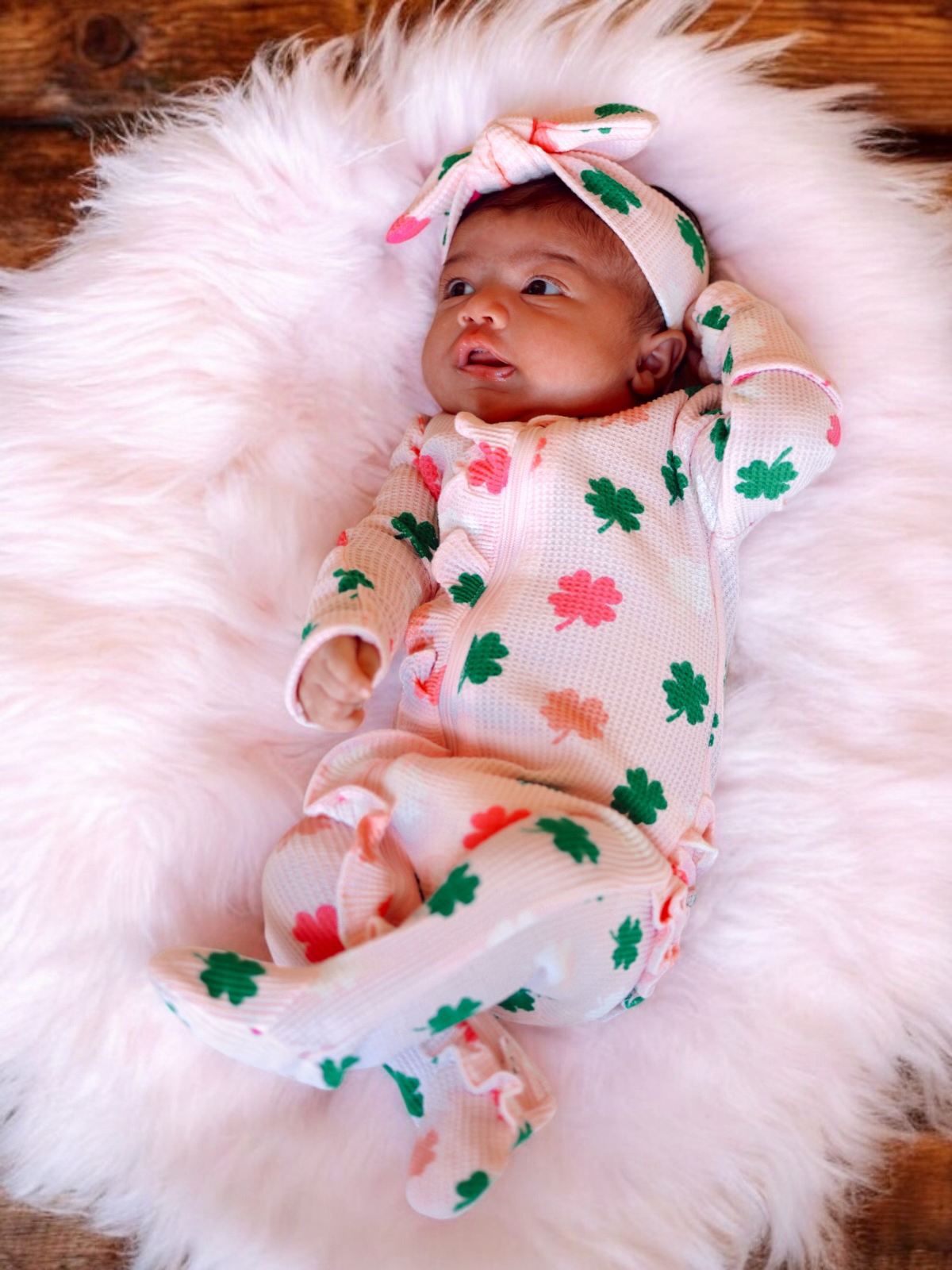Baby girl in floral pajamas and headband, lying on a fluffy blanket, smiling at the camera.