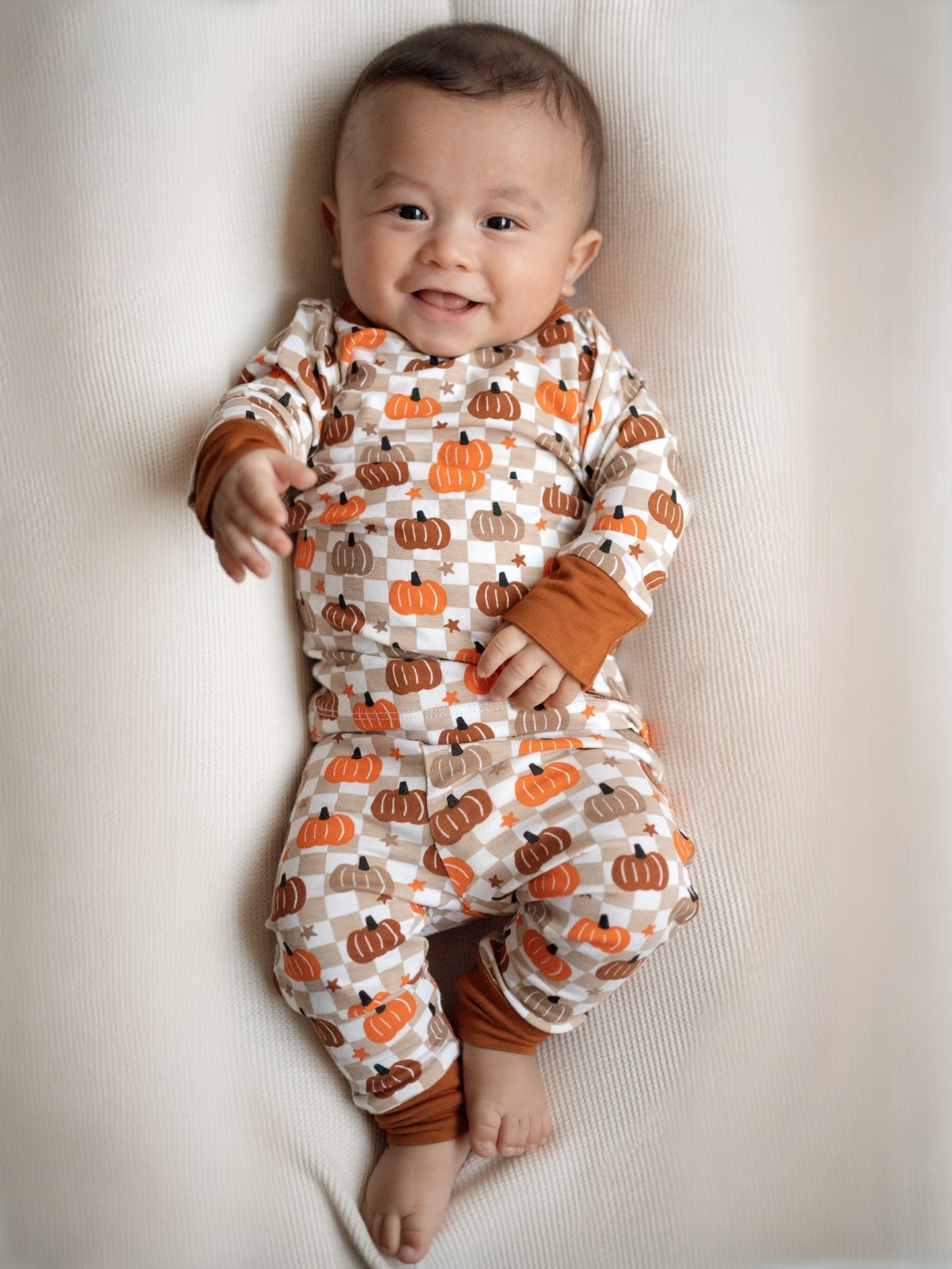 Smiling baby in pumpkin-patterned pajamas on a cozy blanket.
