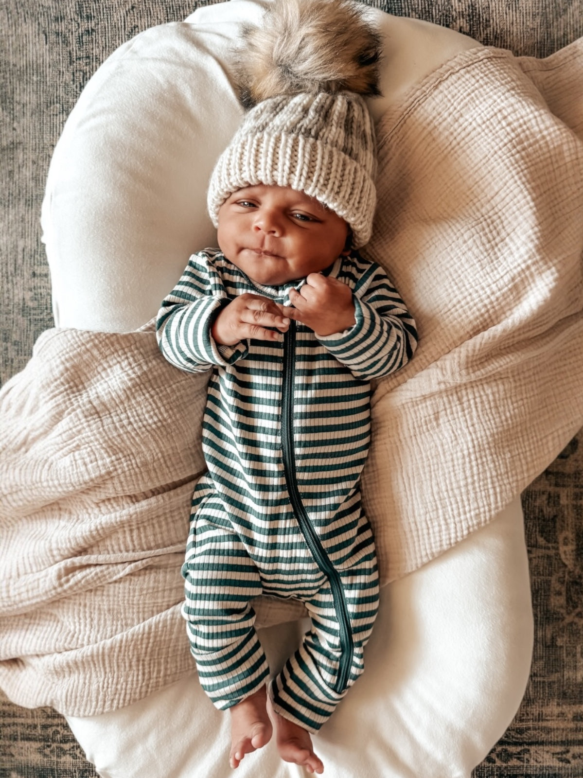 Baby in striped pajamas and knitted hat, lying comfortably on a soft blanket.