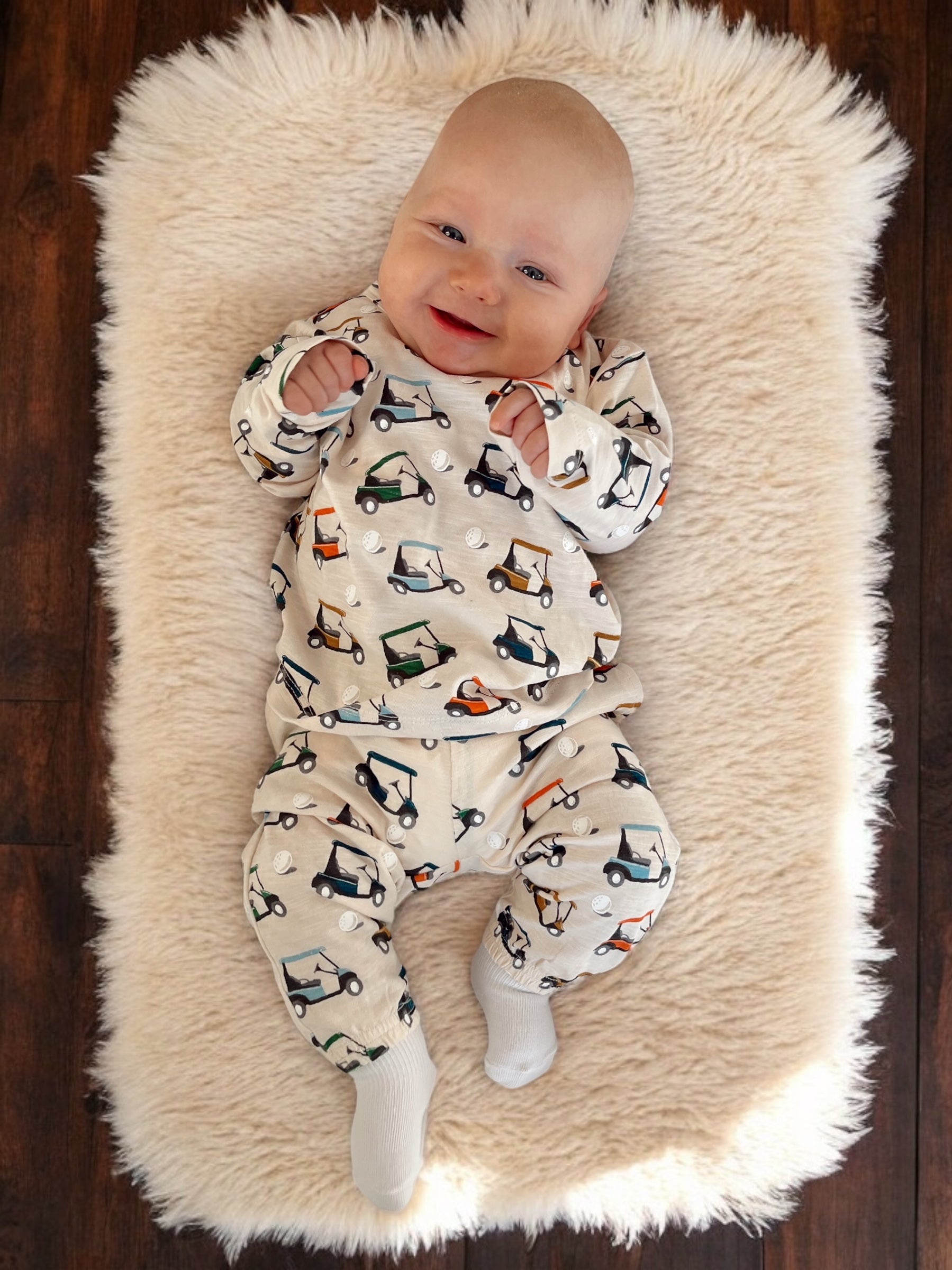 Smiling baby in golf-themed outfit, lying on a fluffy rug, surrounded by a warm, inviting environment.