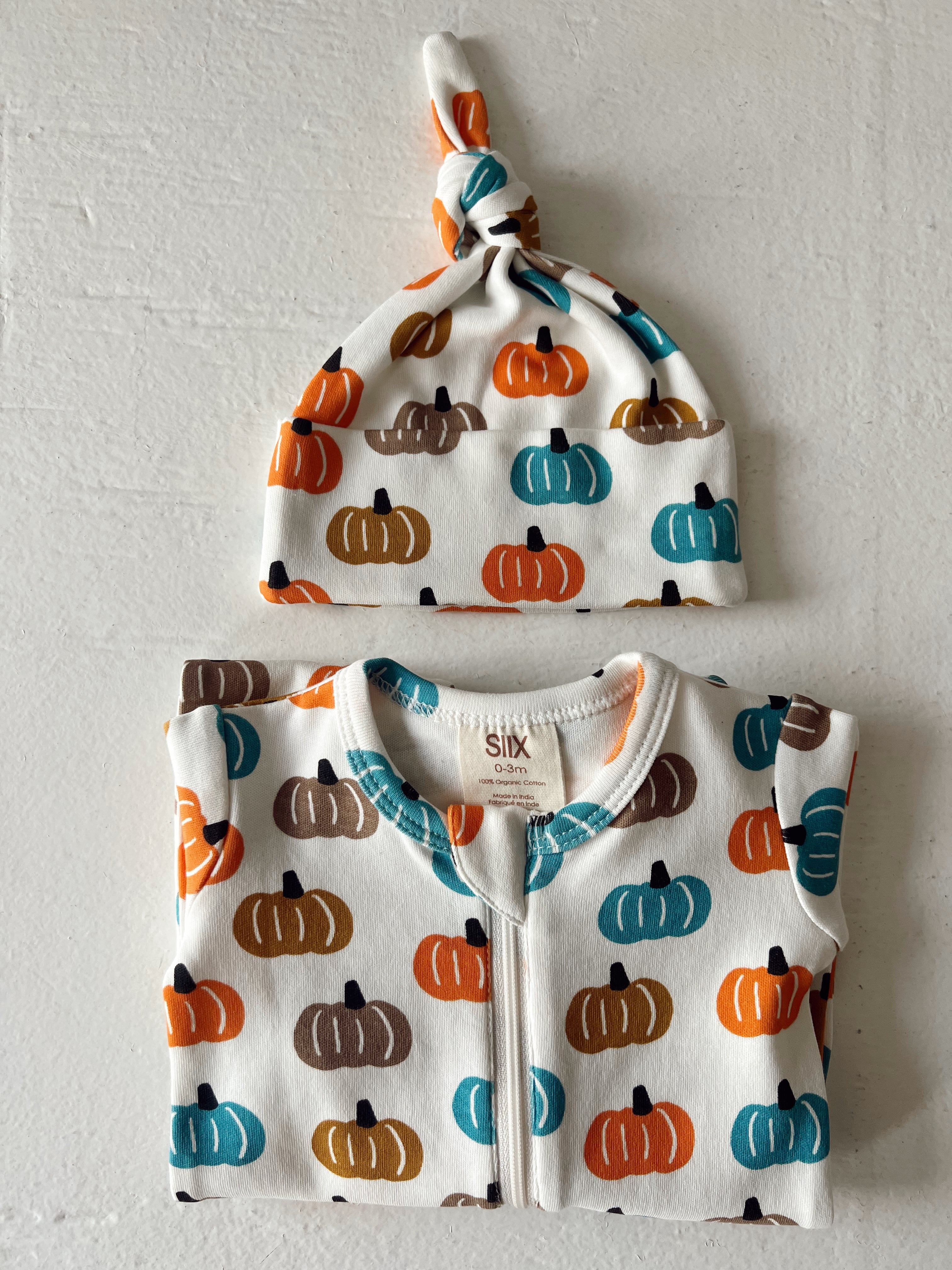 Infant clothing set featuring a pumpkin print onesie and matching knotted hat in autumn colors.
