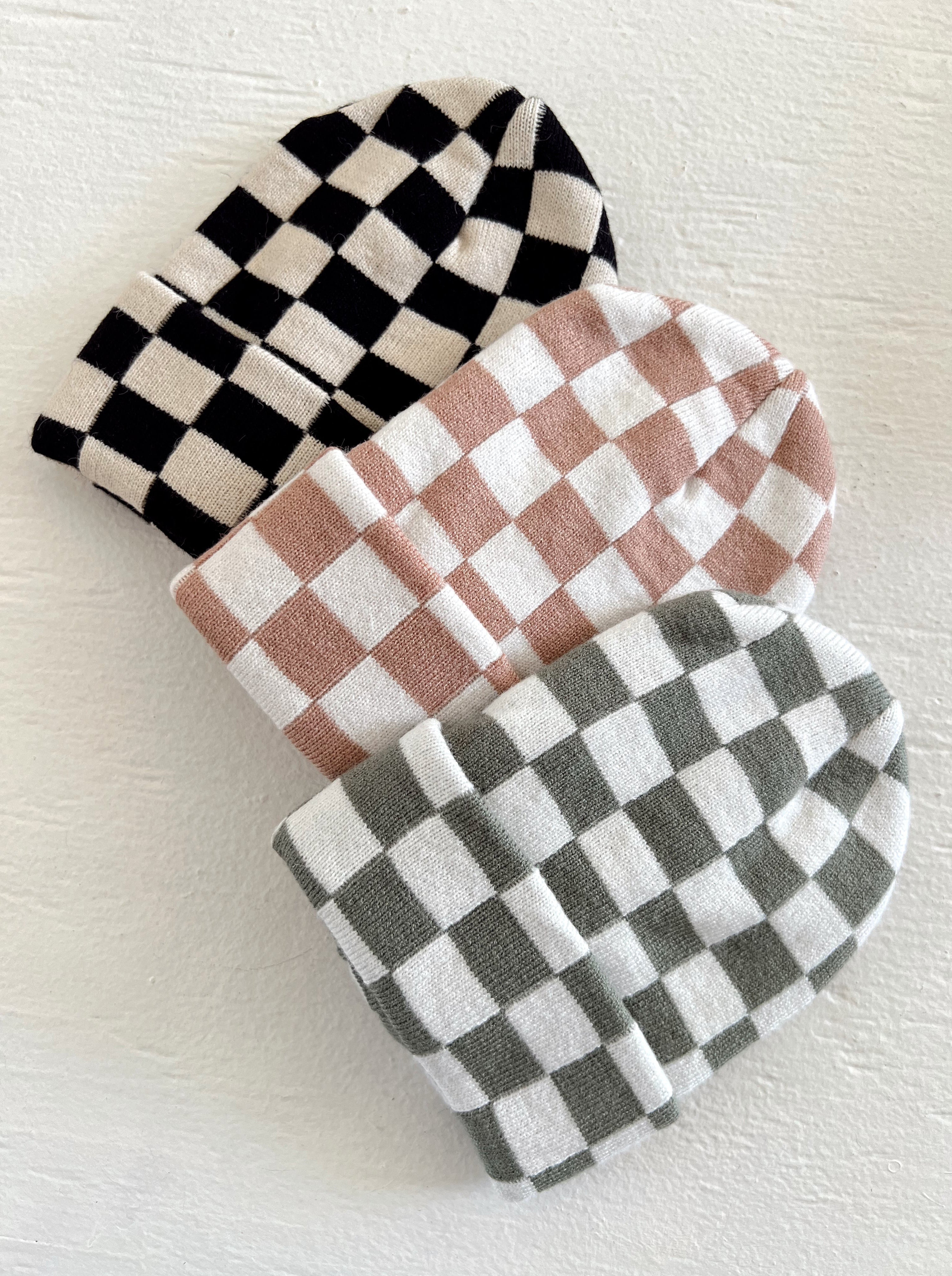 Three checkered beanie hats in black, pink, and green stacked on a white background.