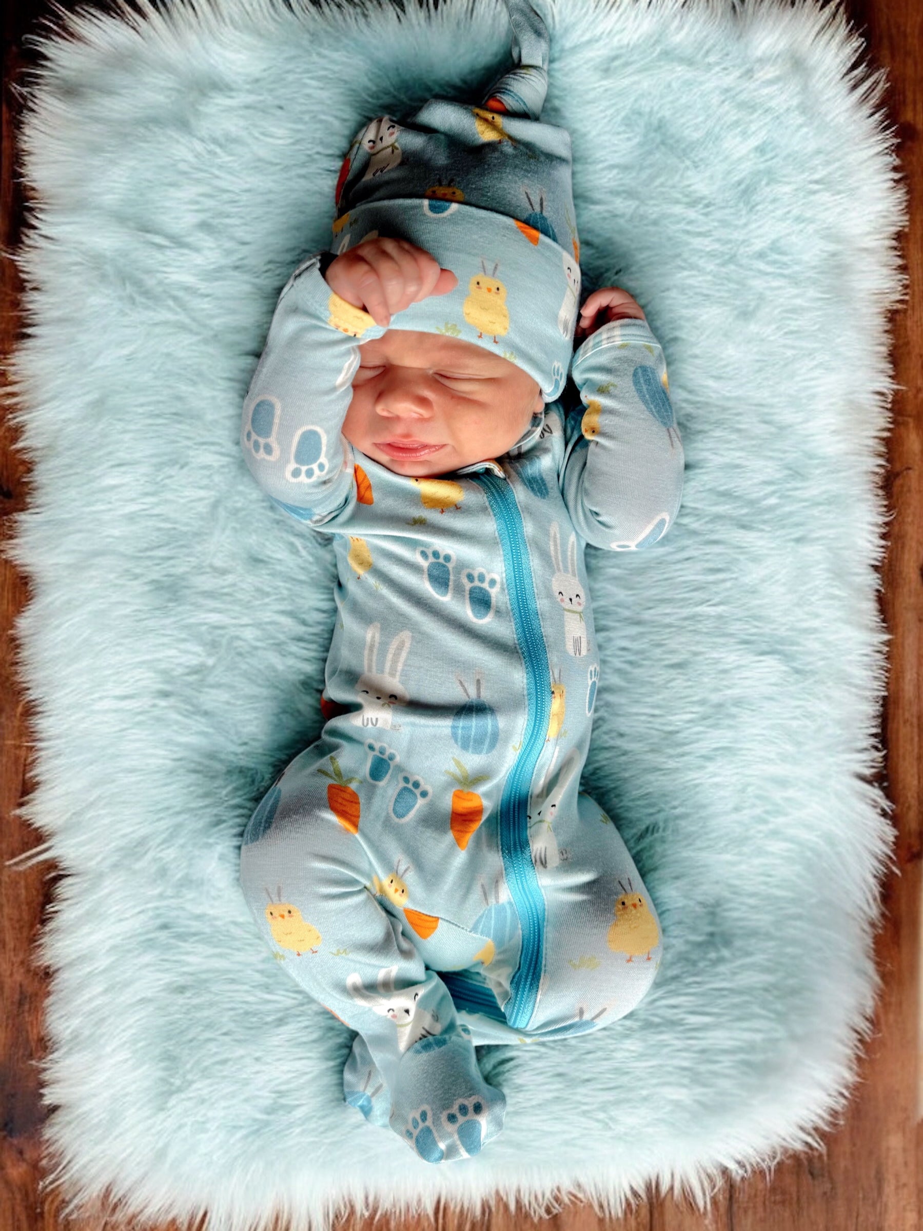 Sleepy baby in a blue patterned onesie and hat, lying on a fluffy light blue blanket.