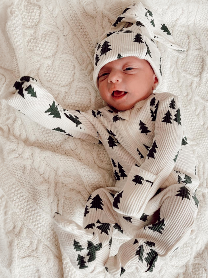 Smiling baby in a cozy, tree-patterned outfit on a knitted blanket.