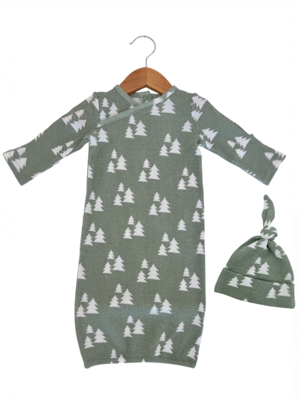 Green baby gown with white tree pattern, accompanied by a matching knot hat, hanging on a wooden hanger.
