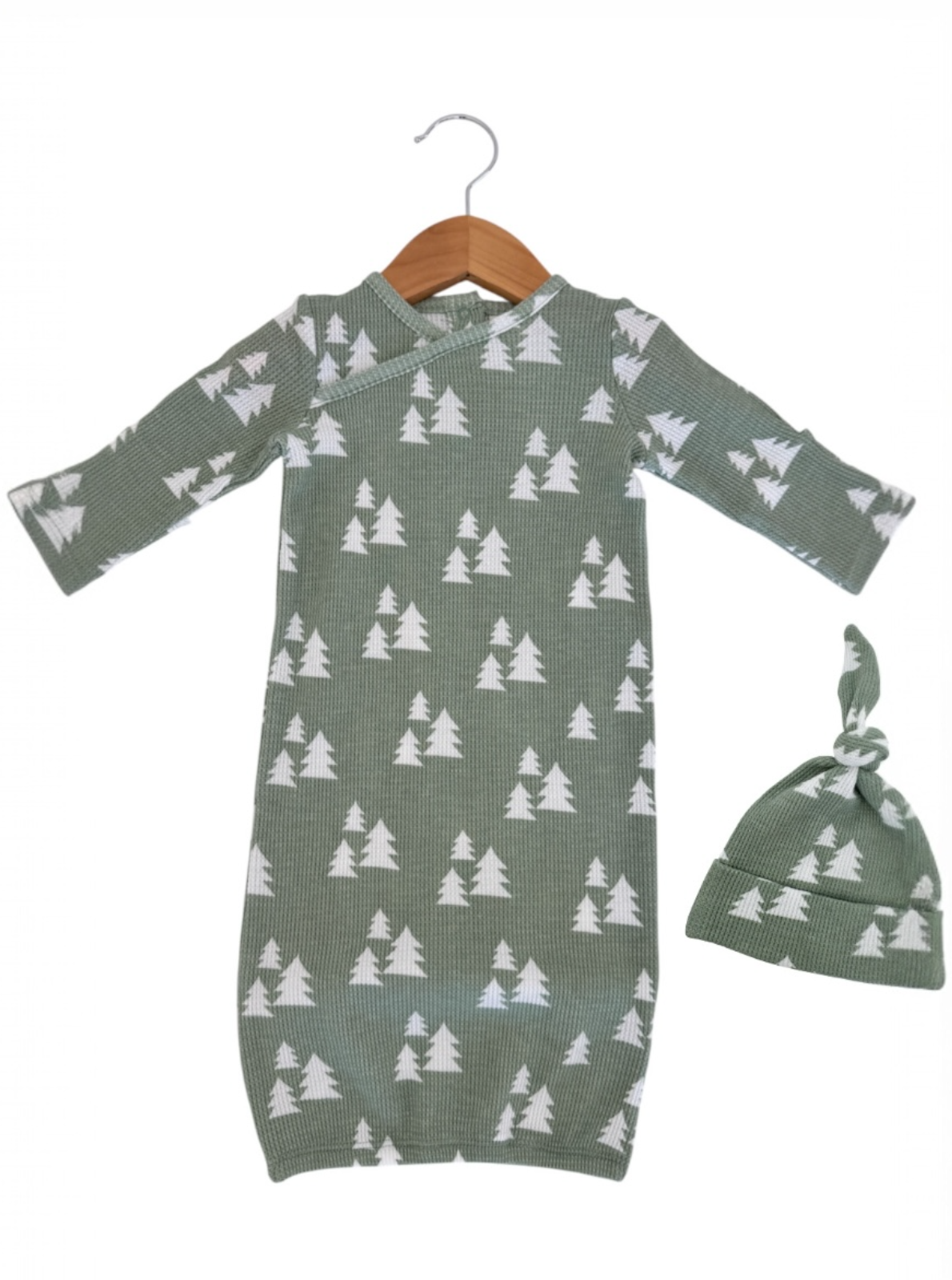 Green baby gown with white tree pattern, accompanied by a matching knot hat, hanging on a wooden hanger.