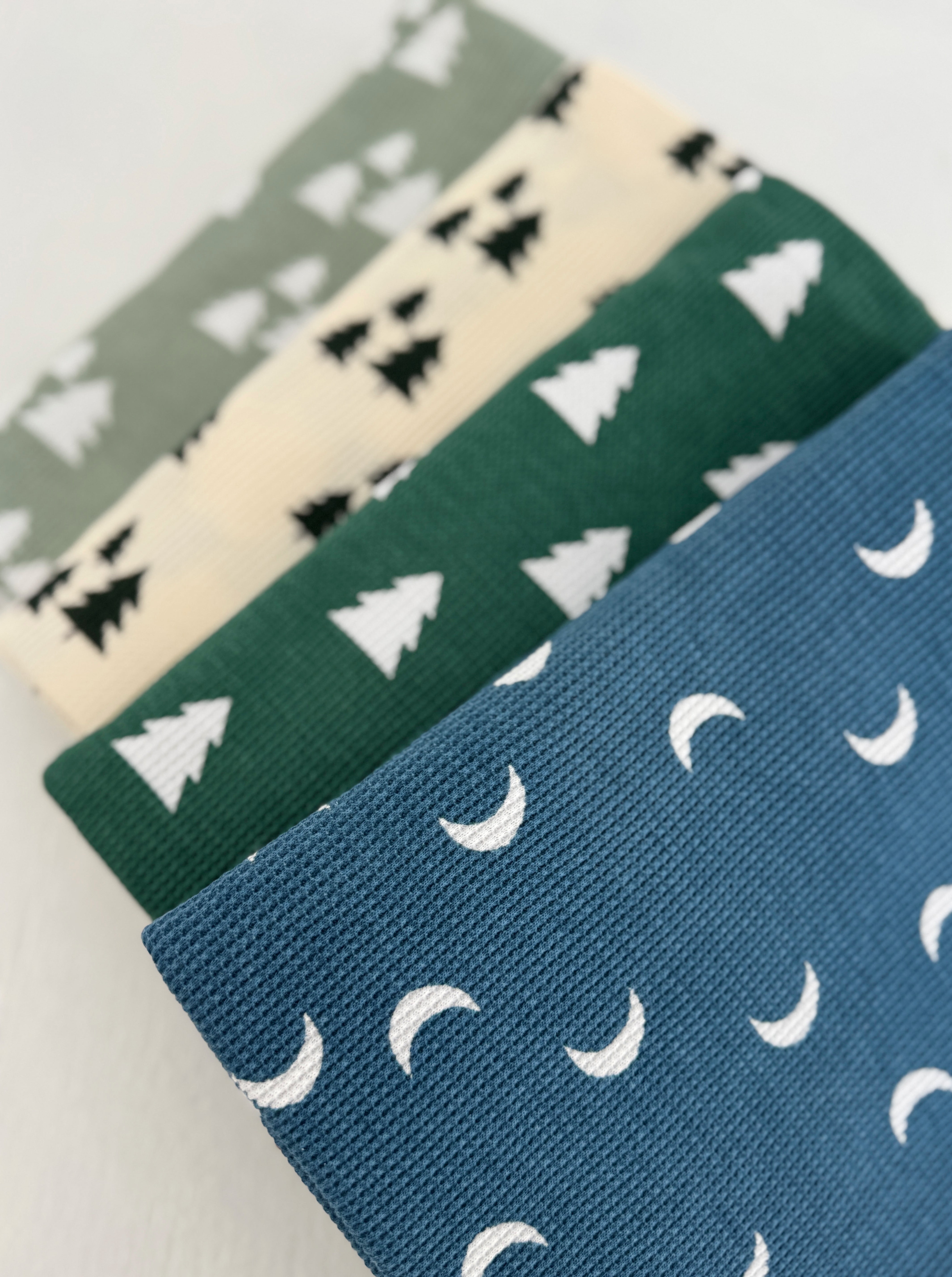 Four fabrics featuring tree and moon patterns in green, blue, cream, and black colors.