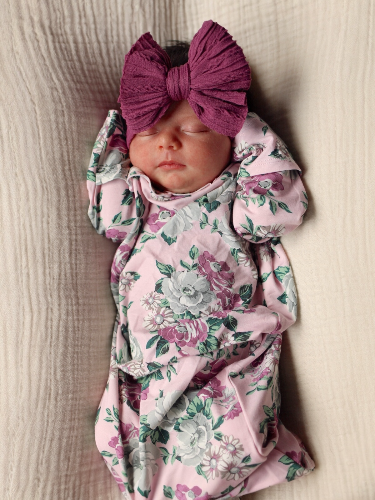 Newborn baby girl in a floral blanket and oversized bow, peacefully sleeping on a soft background.