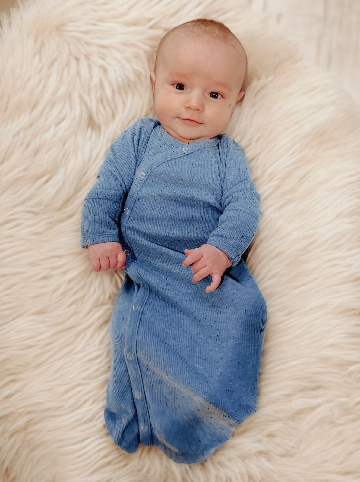 Smiling baby in a blue outfit lying on a fluffy cream blanket.