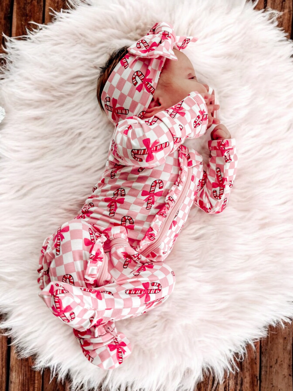 Baby in candy-themed pajamas and headband, resting on a fluffy white rug.