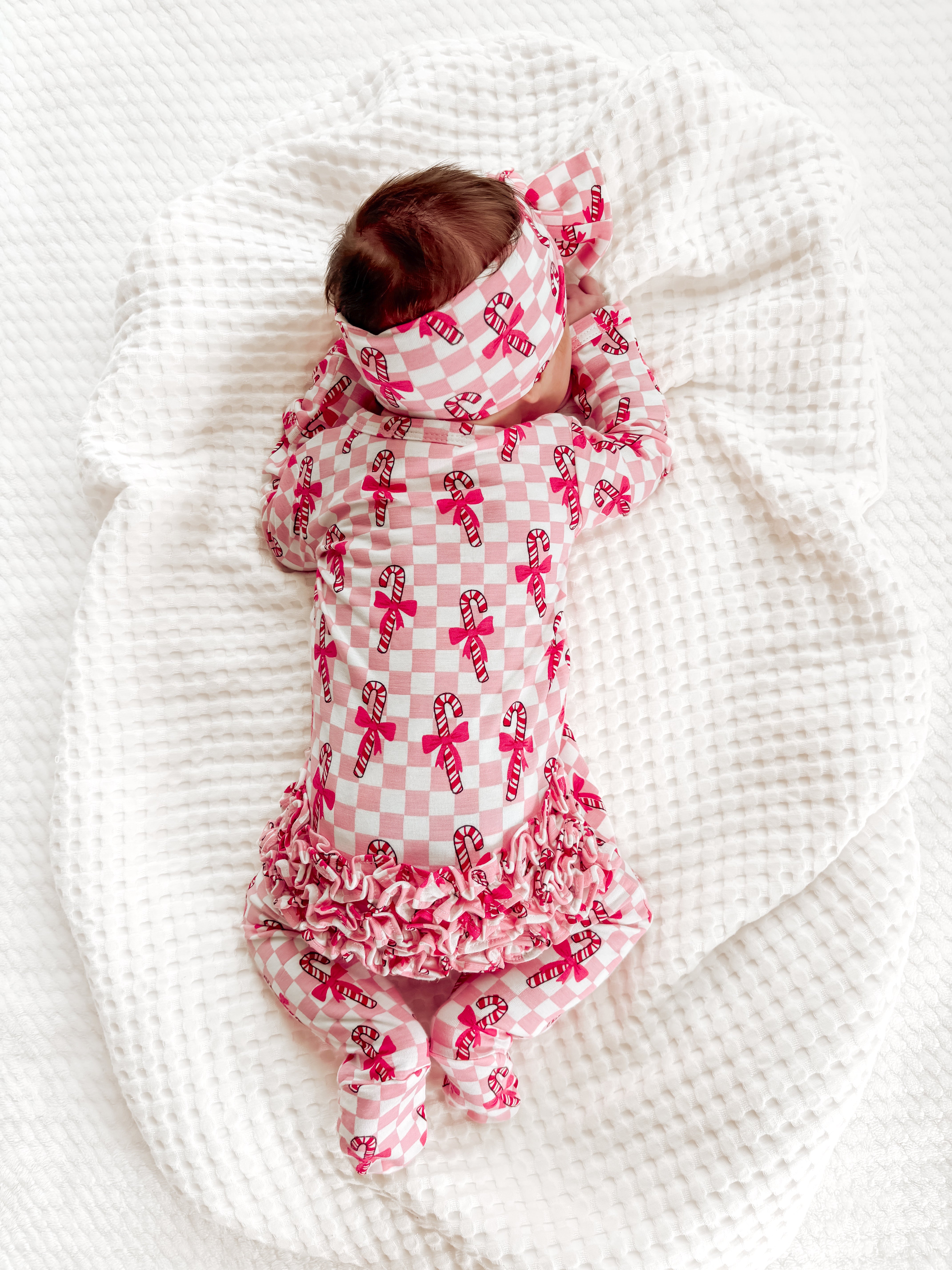 Infant in candy cane print pajamas and headband, napping on a soft, textured blanket.