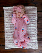Sleeping baby in pink ice cream-themed outfit, resting on a soft blanket on wooden floor.