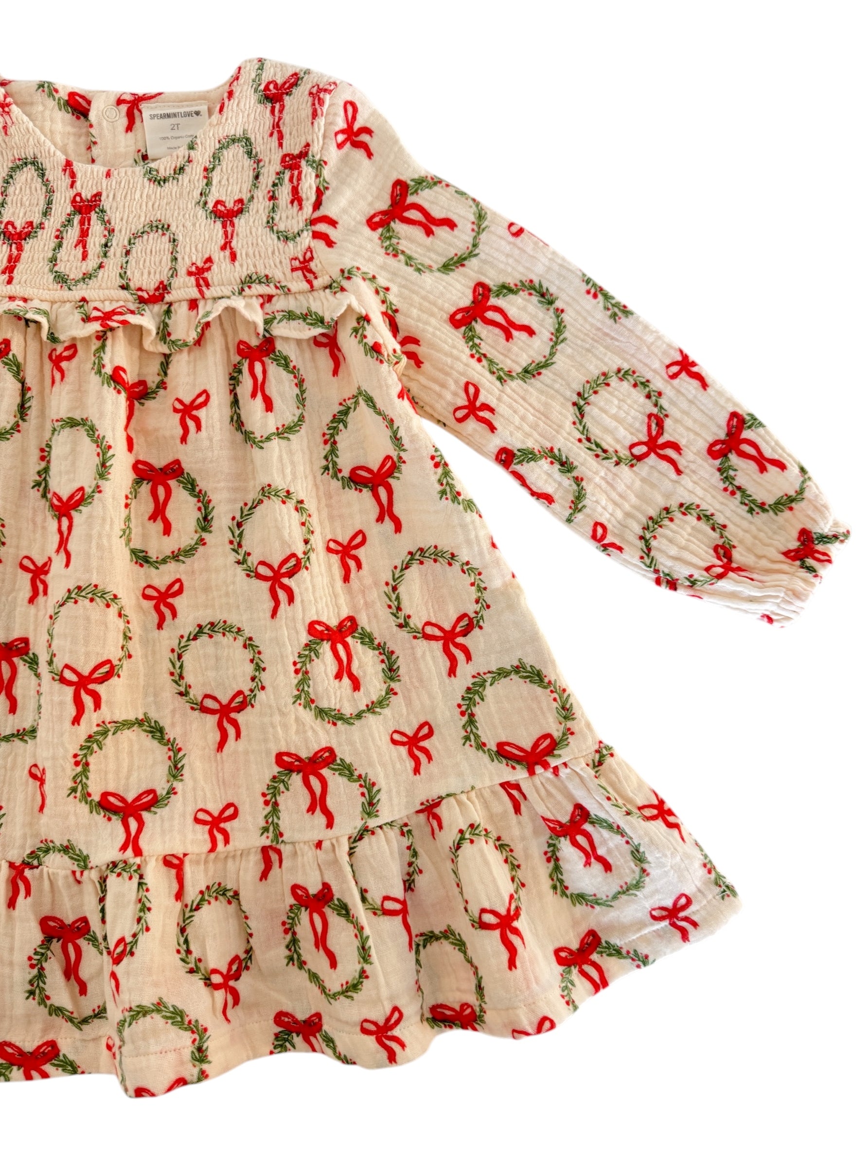 Cream dress with red bows and green wreaths, long sleeves, and ruffled hem, perfect for festive occasions.