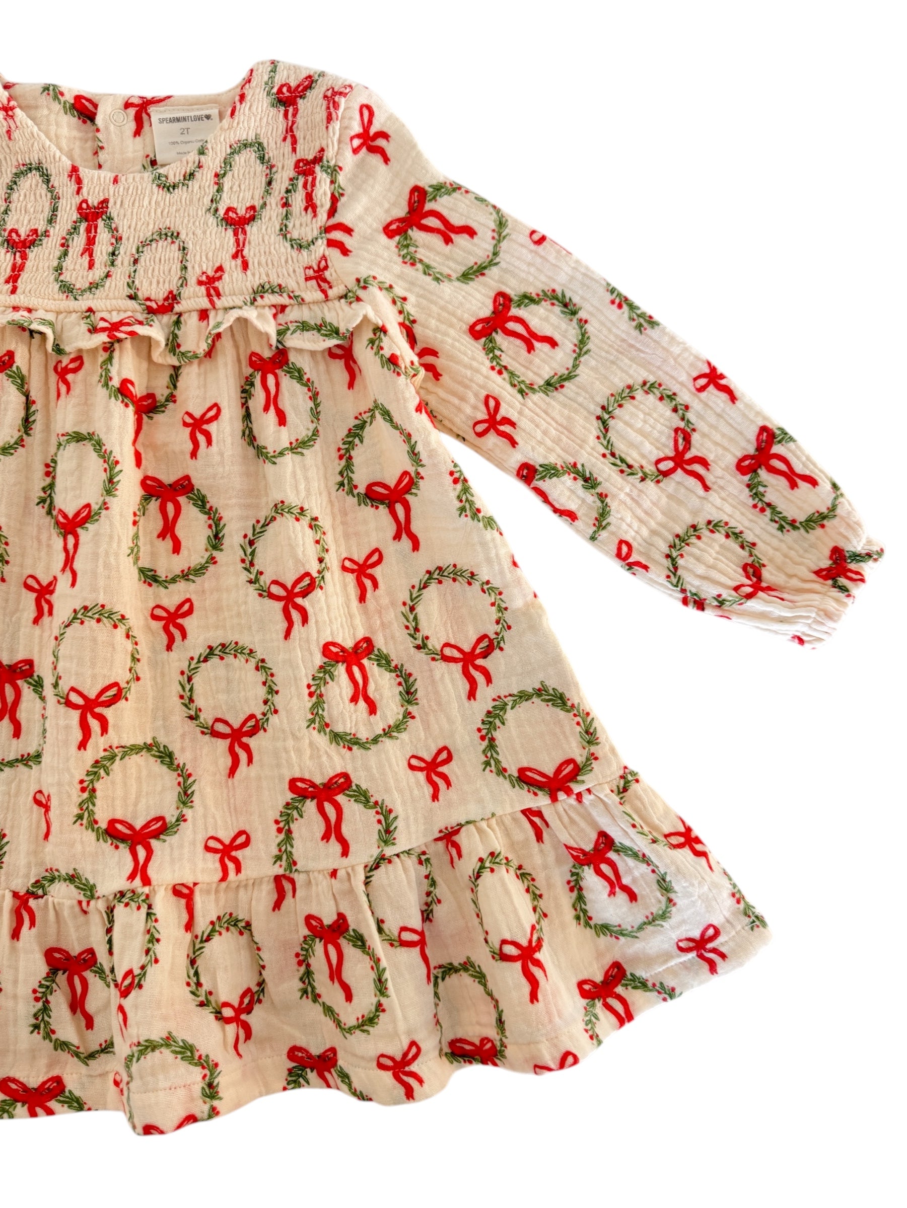 Cream dress with red bows and green wreaths, long sleeves, and ruffled hem, perfect for festive occasions.