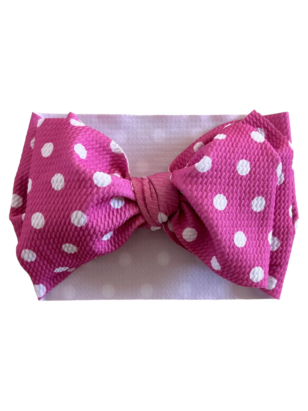 Pink polka dot bow headband on a soft pink background, perfect for stylish accessories.