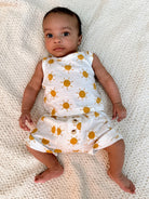 Infant lying on a fluffy blanket, wearing a sun-patterned outfit, with big expressive eyes.